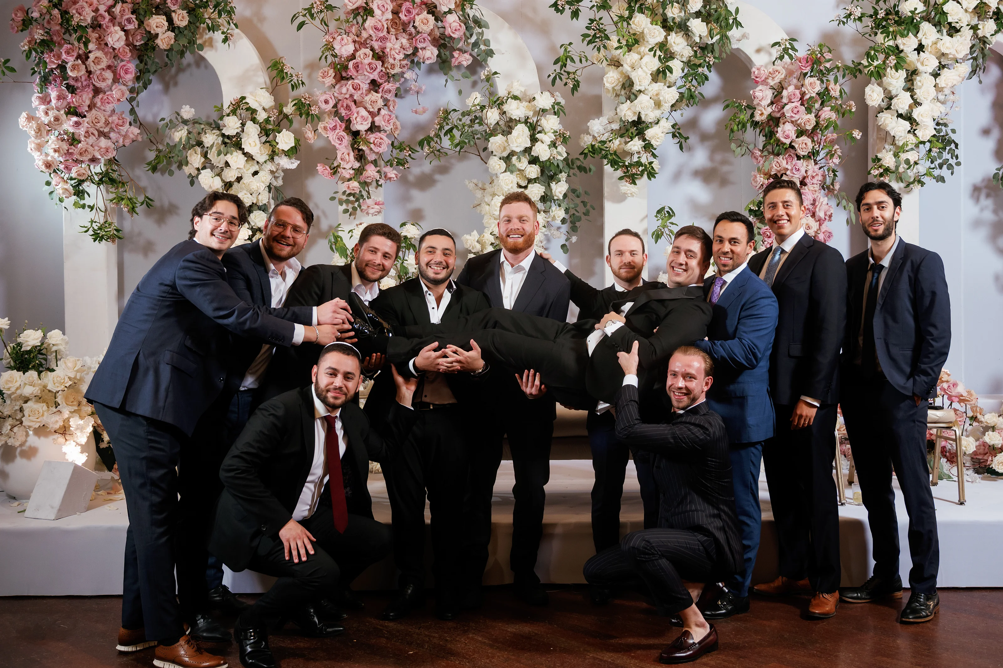 Posed group portrait of close family members in suits in front of large floral arches with pink and white roses.