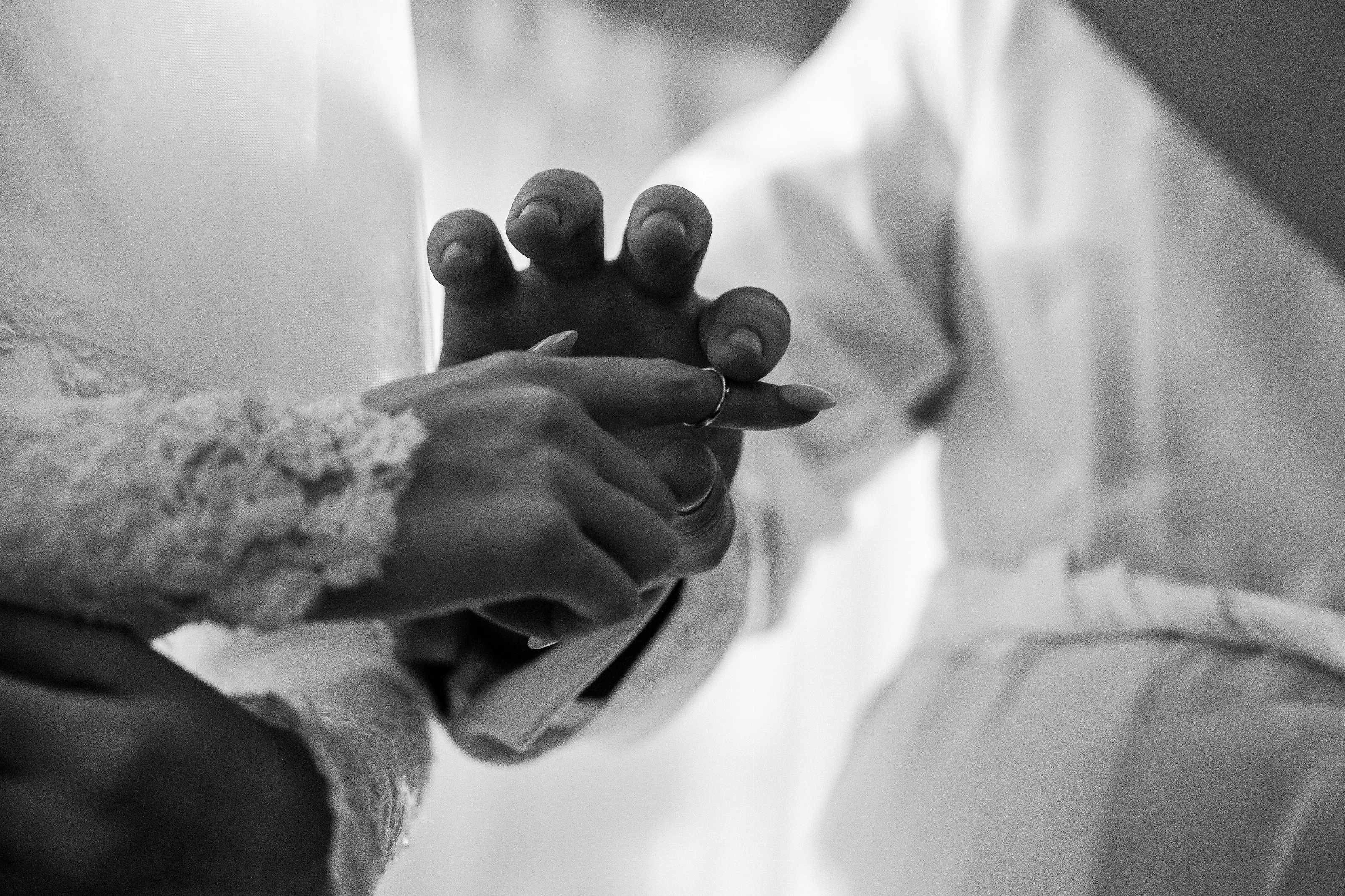 Black-and-white close-up of intertwined hands with a ring during a Jewish wedding ritual, softly blurred background.
