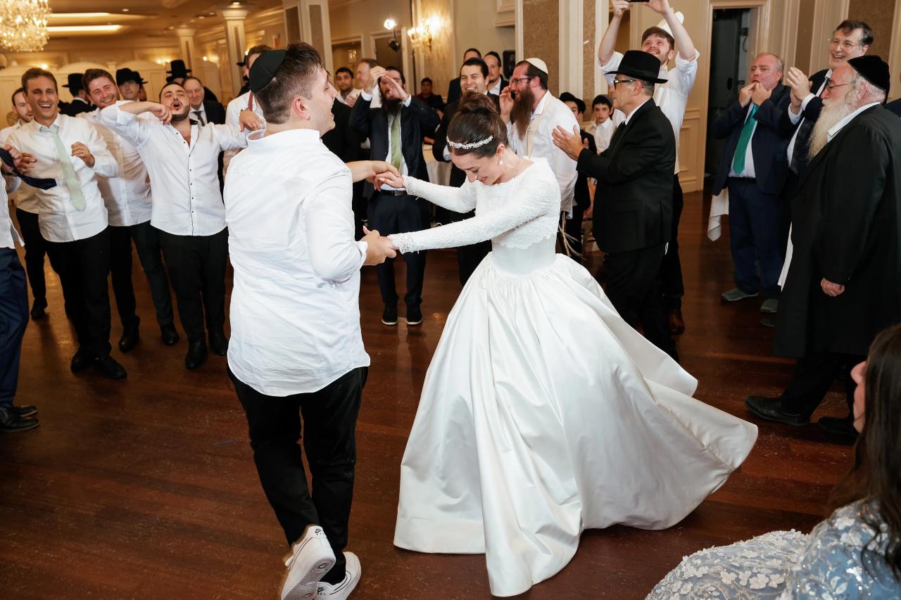 Bride and groom dancing in a ballroom with their celebration sweeping across the floor as guests clap and watch.