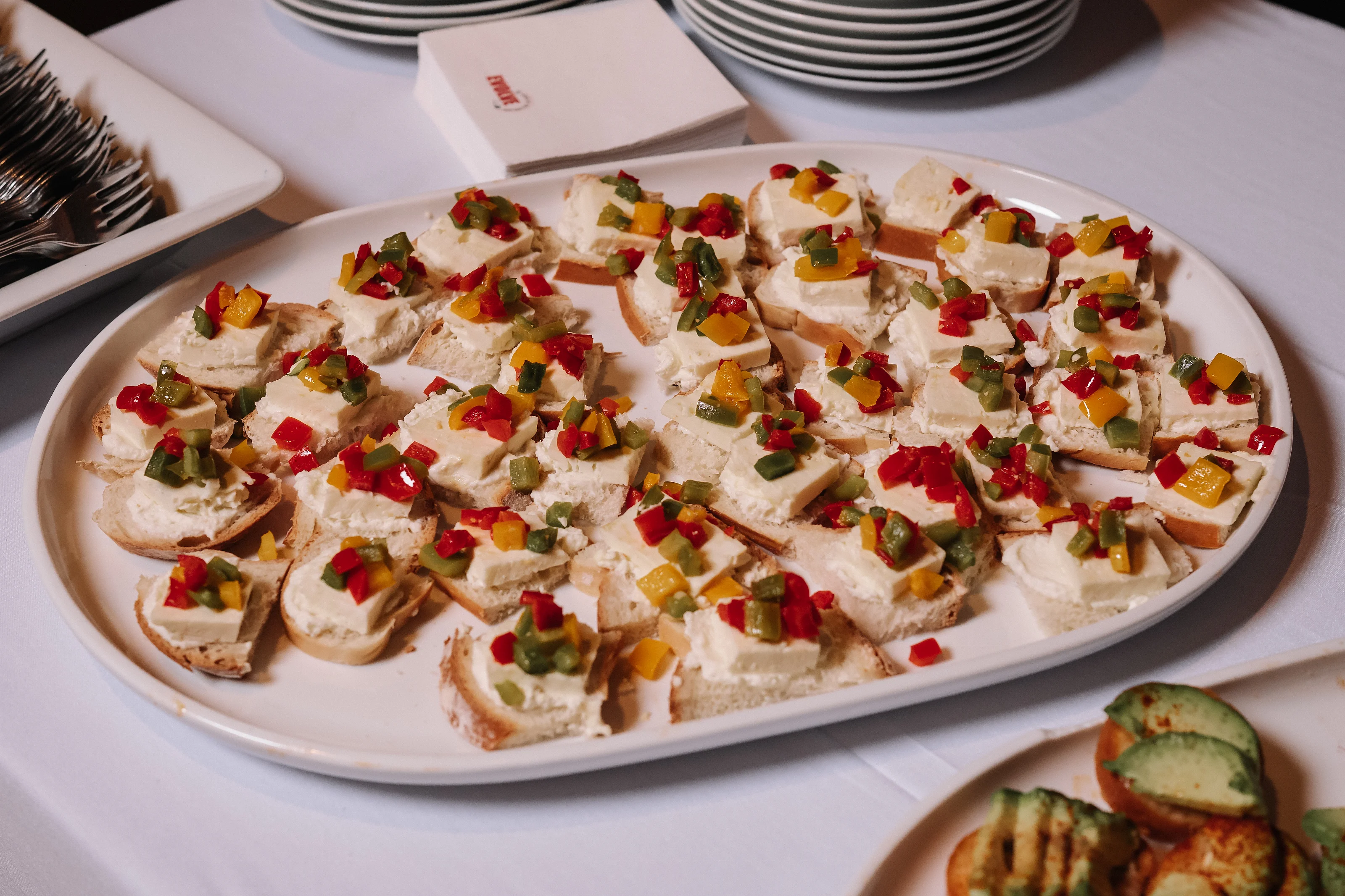 Close-up of a reception platter with bite-size canapés topped with chopped red, yellow, and green garnishes.