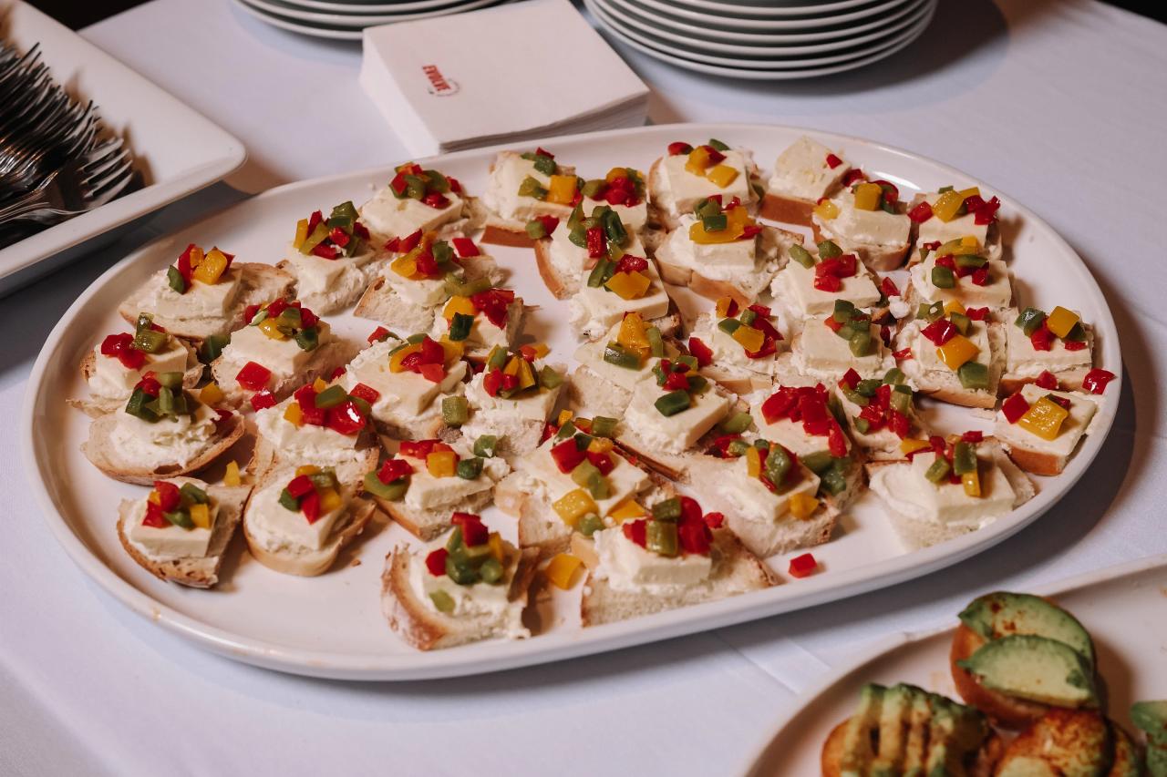 Close-up of a reception platter with bite-size canapés topped with chopped red, yellow, and green garnishes.