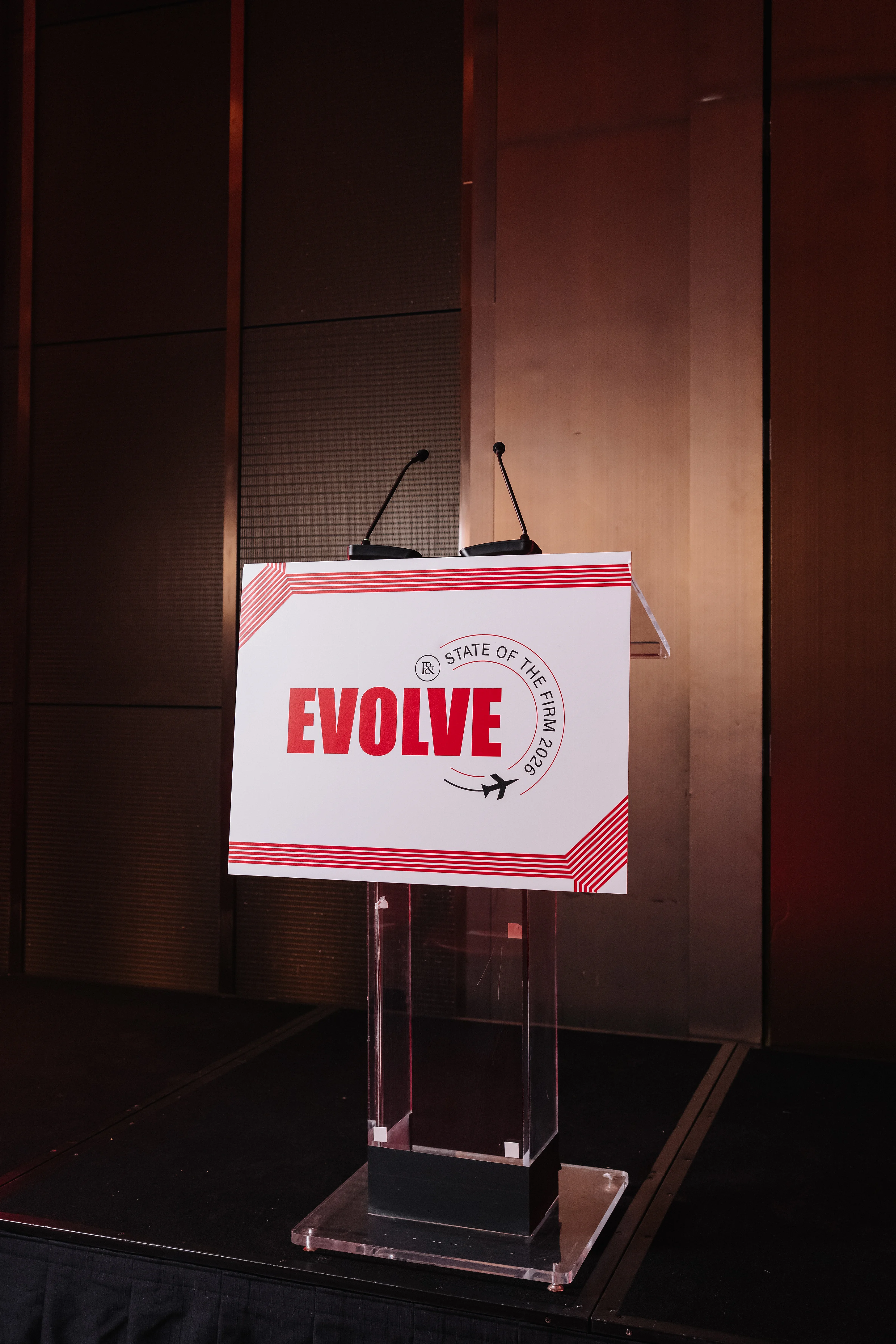 Red-and-white “EVOLVE” sign on an event podium with two microphones against a dark indoor backdrop
