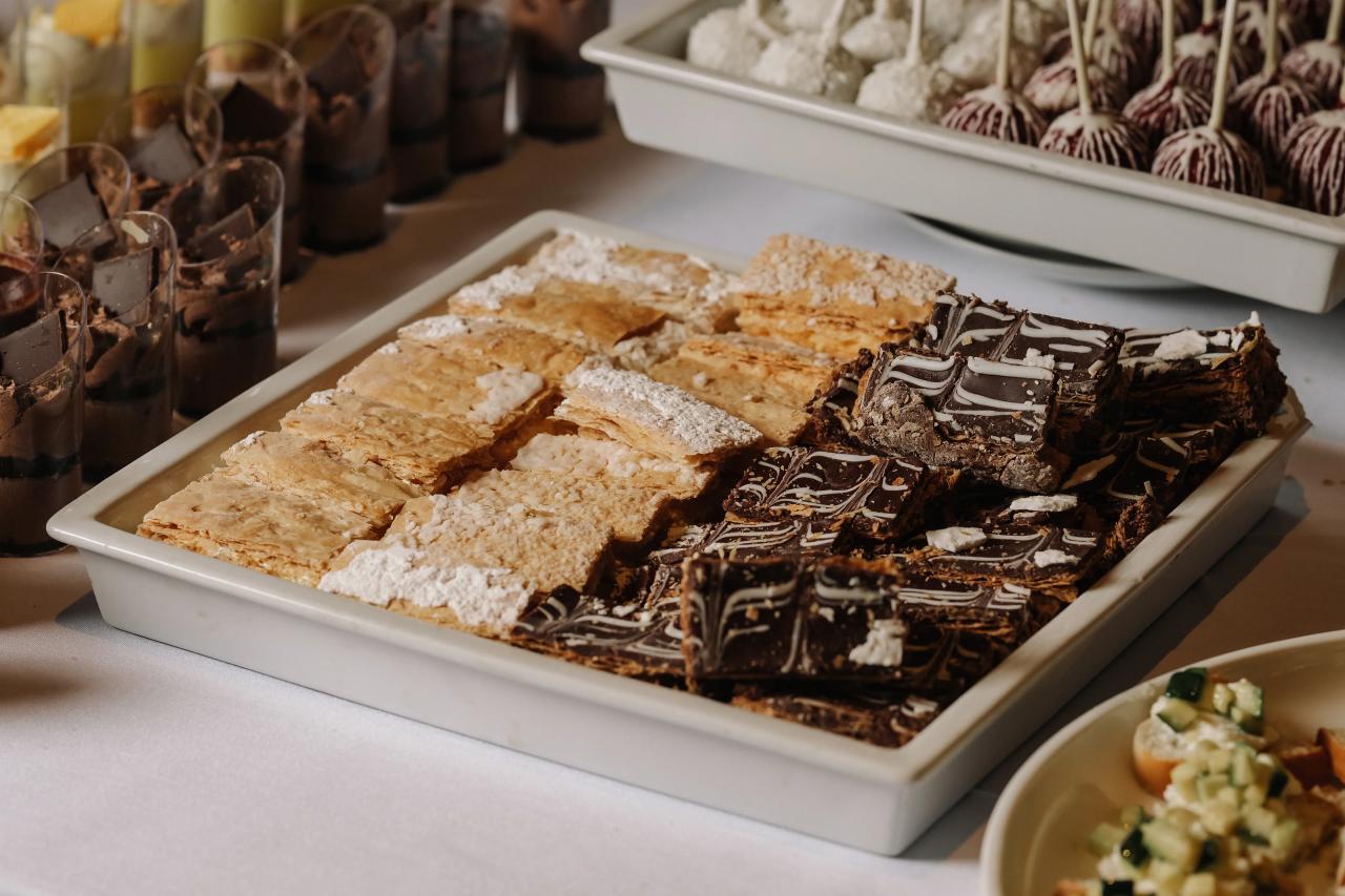 Close-up of an assortment of desserts in a white serving tray with chocolate-topped pieces and warm reception lighting