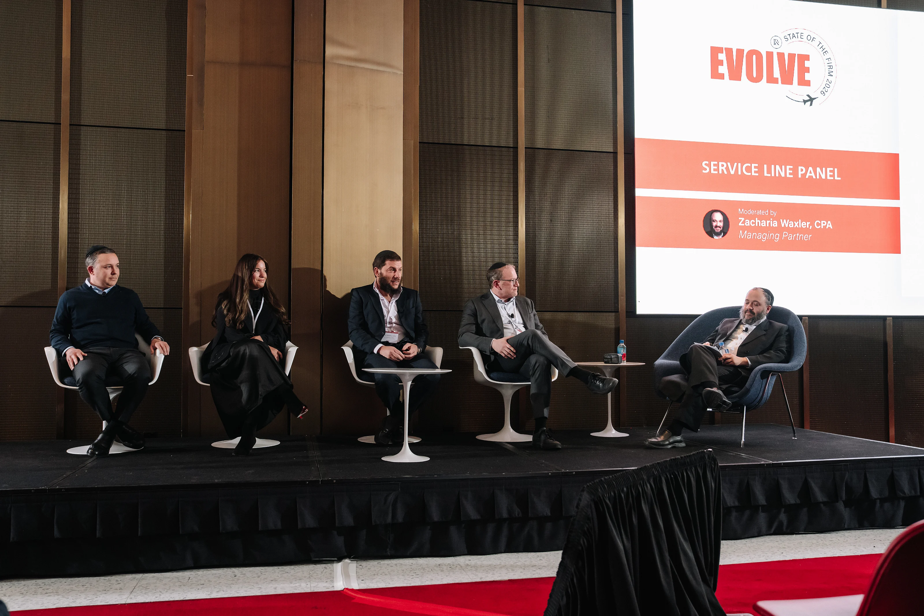 Seated panelists on a stage in front of a large screen reading “SERVICE LINE PANEL,” photographed during a conference panel discussion.
