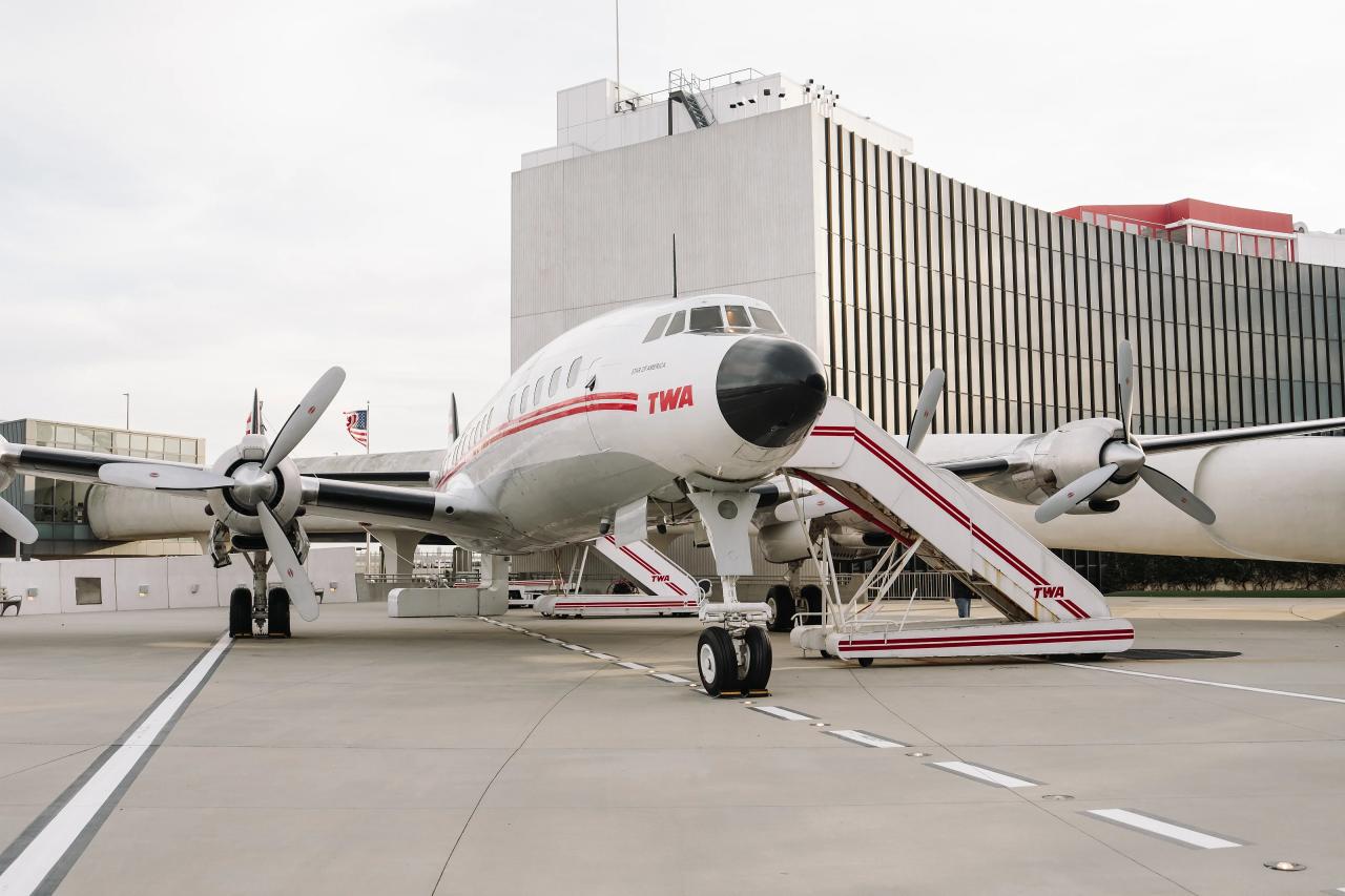 Wide view of a passenger airplane parked at an airport gate beside a terminal building.