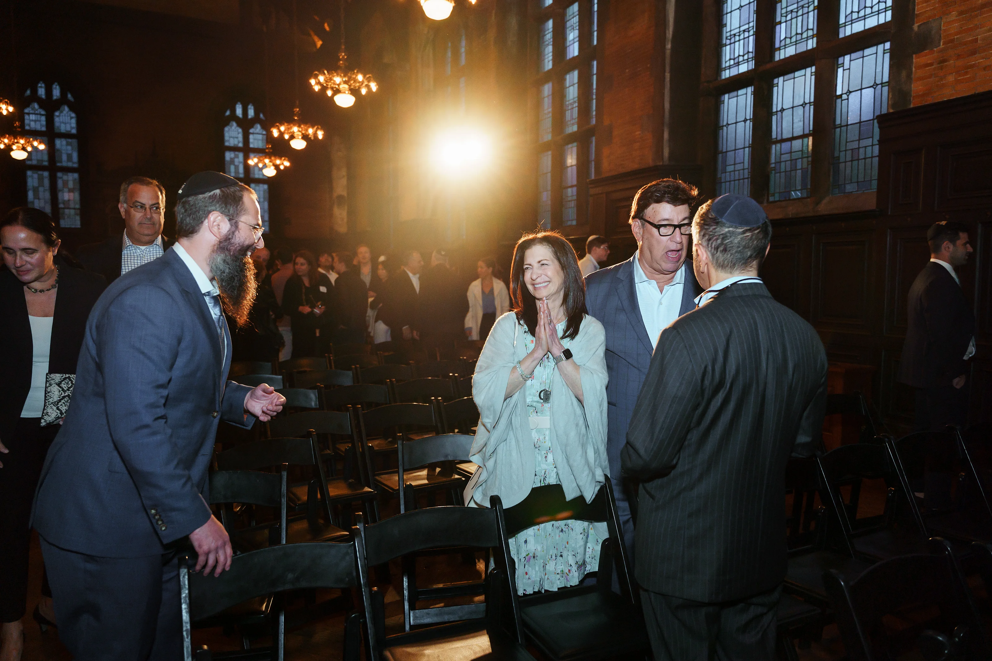 Guests celebrating and laughing during a wedding reception, illuminated by bright chandelier light and a warm halo effect in a historic hall.