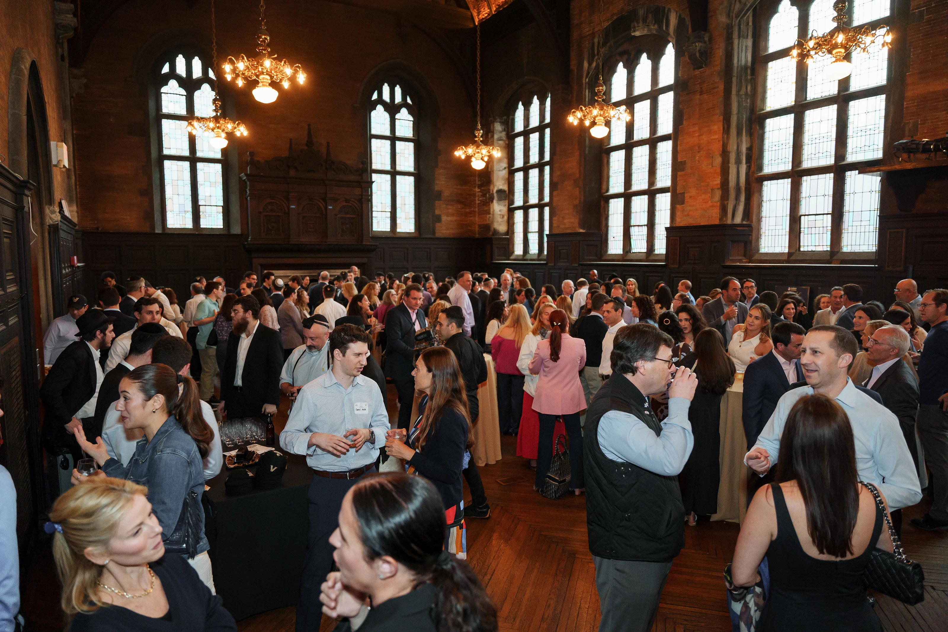 Wedding celebration in a large historic hall with warm chandeliers as guests mingle and converse.