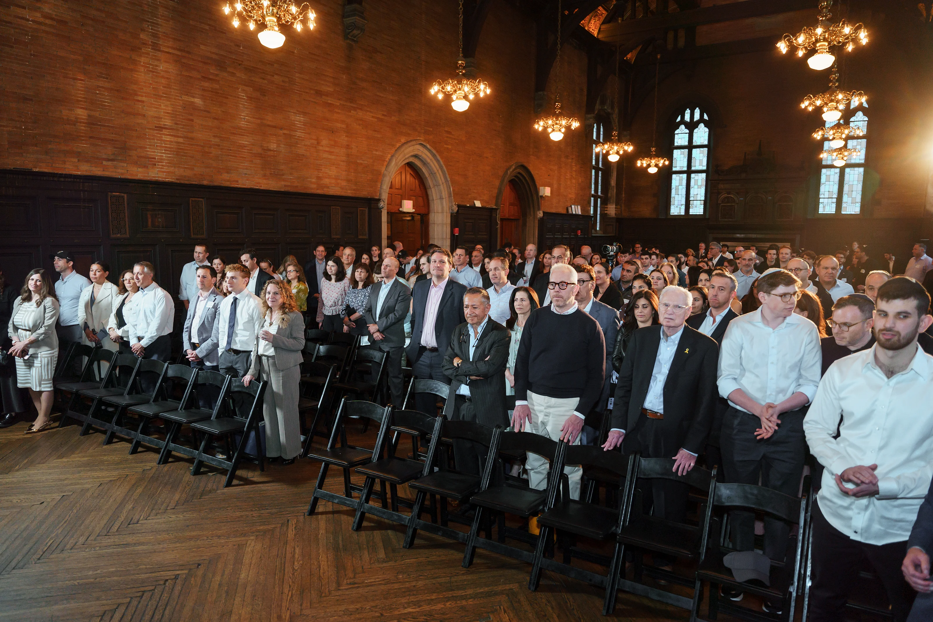 Warm chandelier-lit ceremony hall with guests seated in rows facing forward, captured in a wide angle perspective.