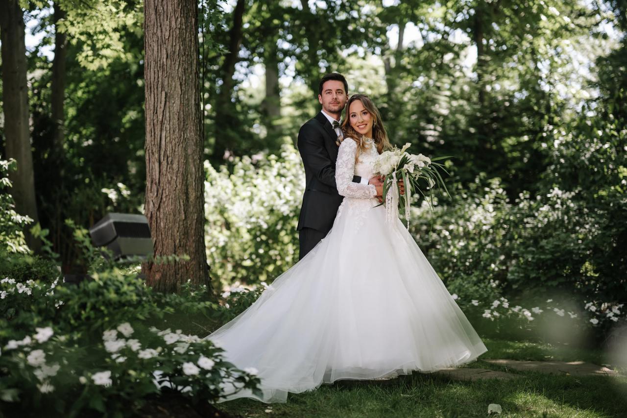Wedding couple standing together outdoors in a garden, the bride holding a bouquet with a flowing veil while trees and greenery fill the background. Wedding at Crystal Plaza, Livingston, NJ.