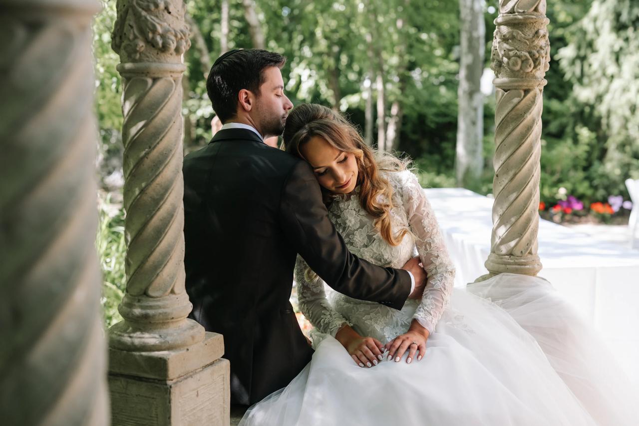 Wedding couple embracing closely outdoors beside stone columns, with the bride leaning into the groom during a quiet emotional moment. Wedding at Crystal Plaza, Livingston, NJ.