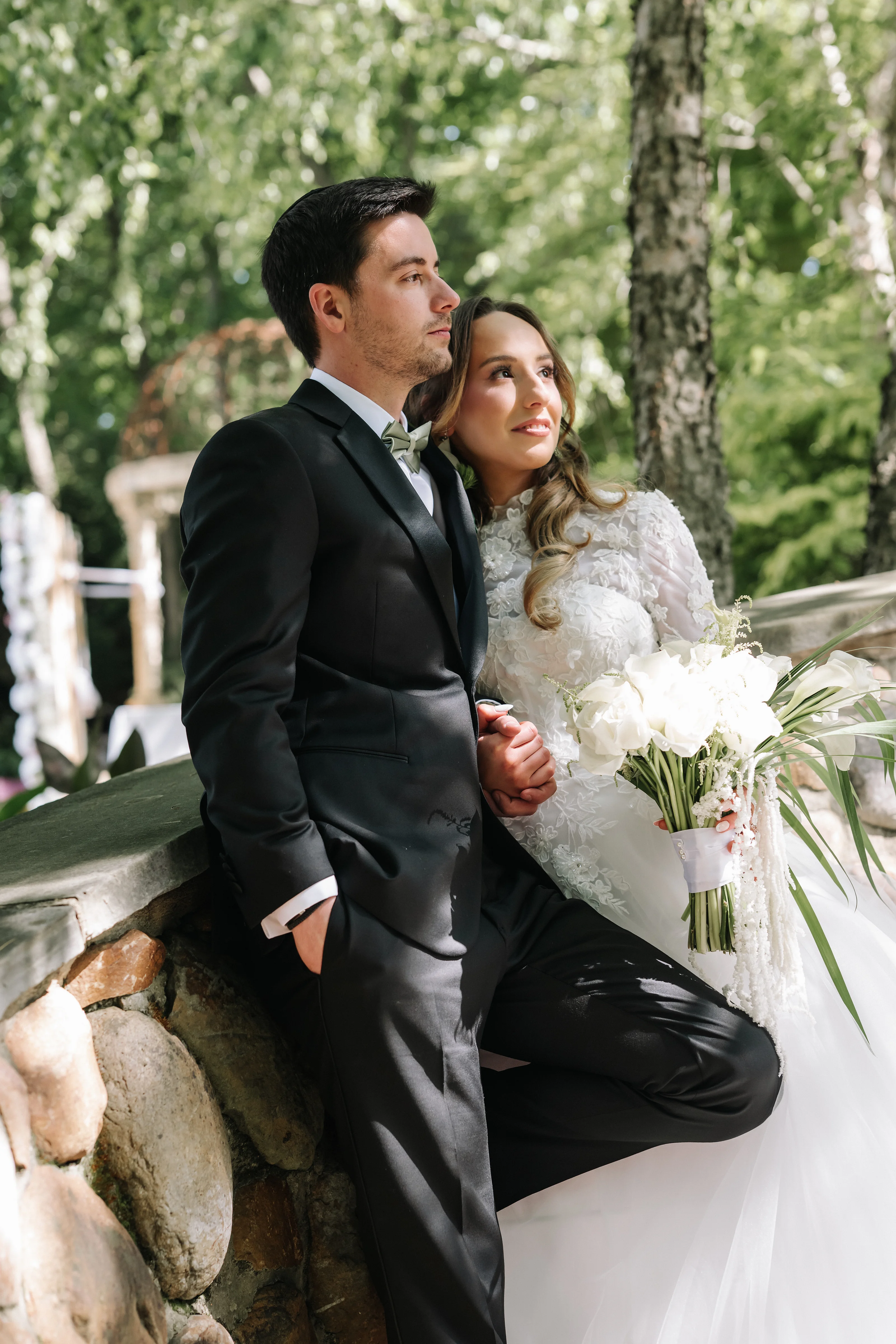 Couple seated outdoors during their wedding day, the bride holding a bouquet while they share a quiet, affectionate moment.