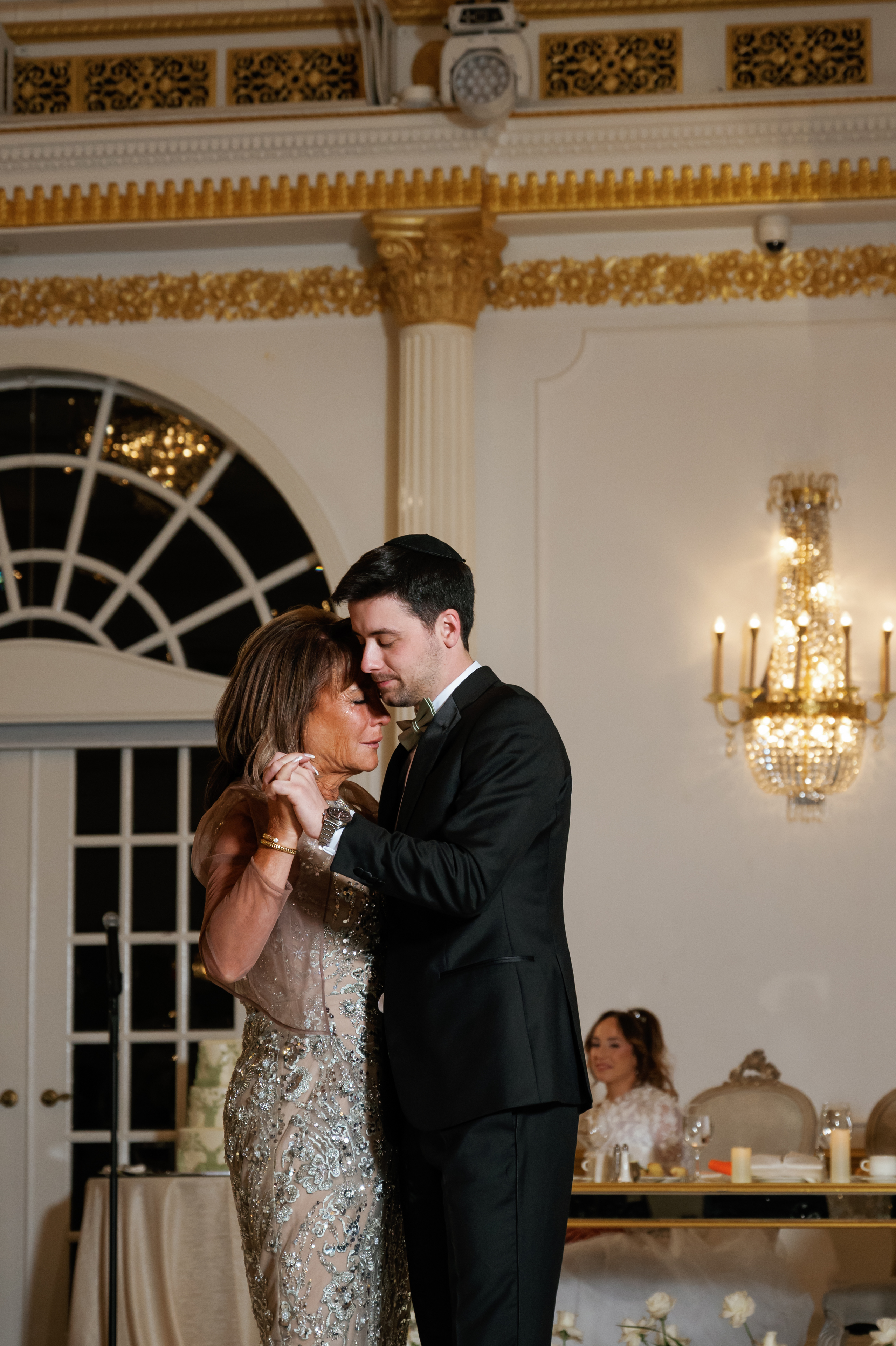 Couple sharing an intimate embrace during a warm-lit wedding reception indoors.