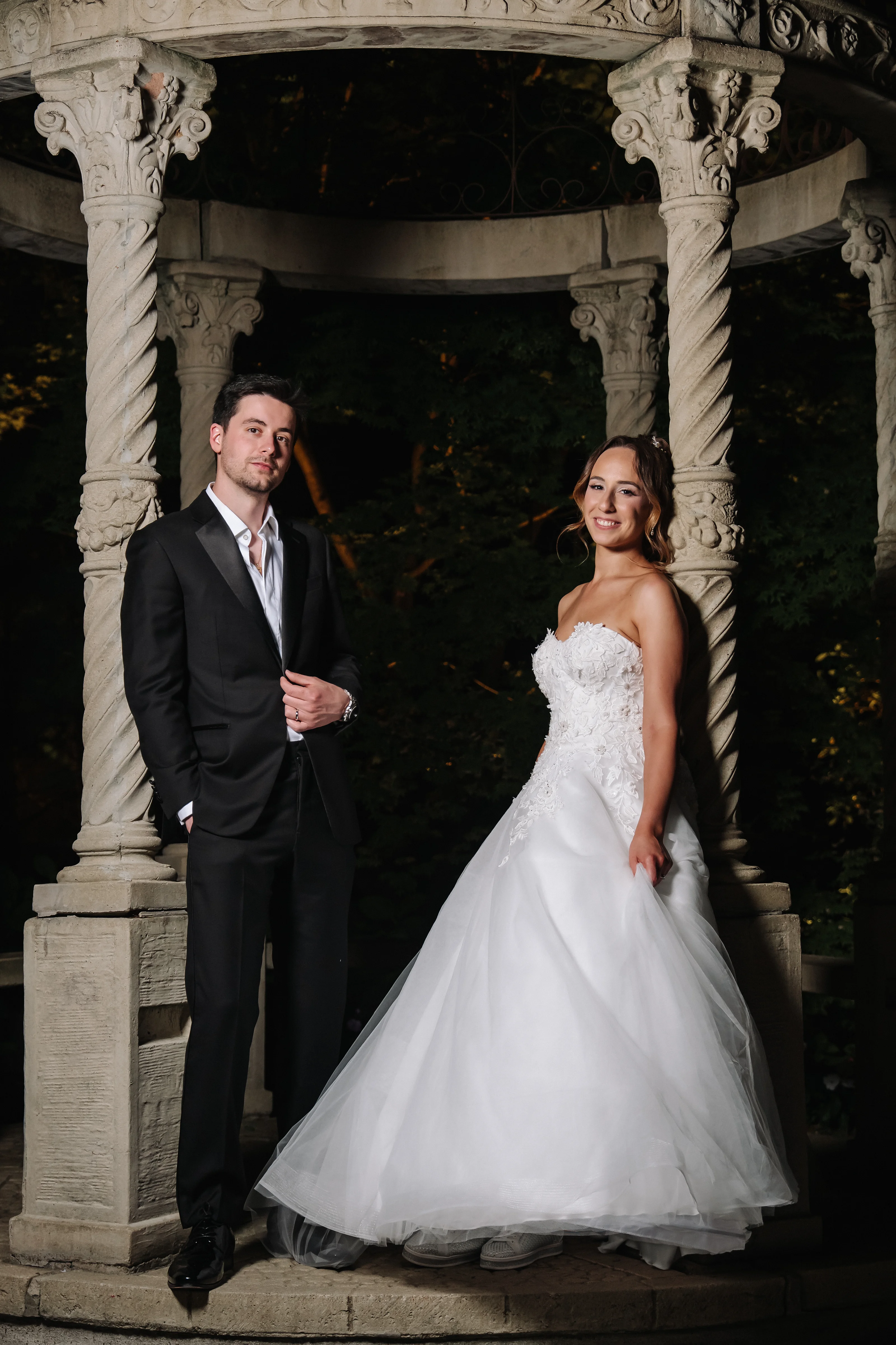Bride and groom posed under ornate stone arches at night during a wedding portrait session.