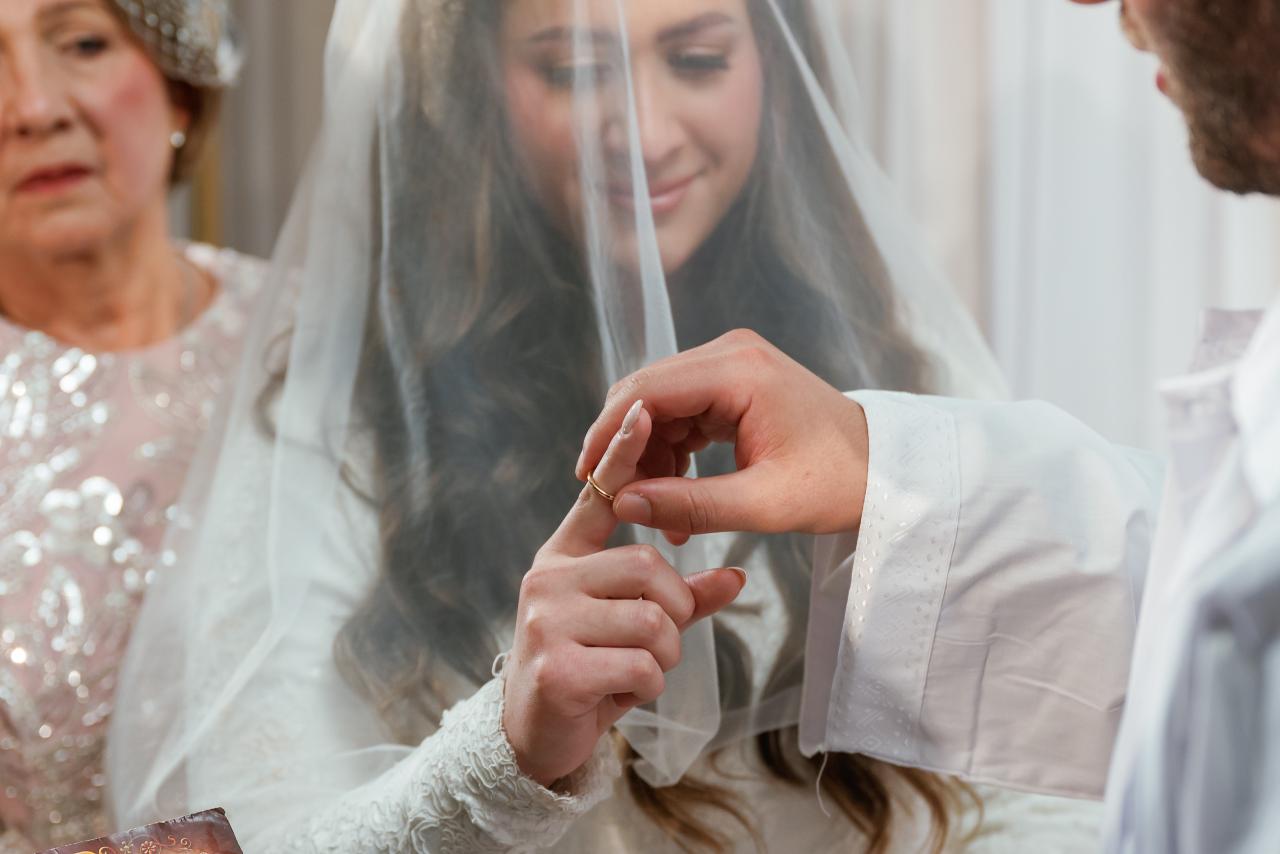 Hands adjusting a sheer wedding veil, with the bride’s smiling face softly visible behind the gauze.