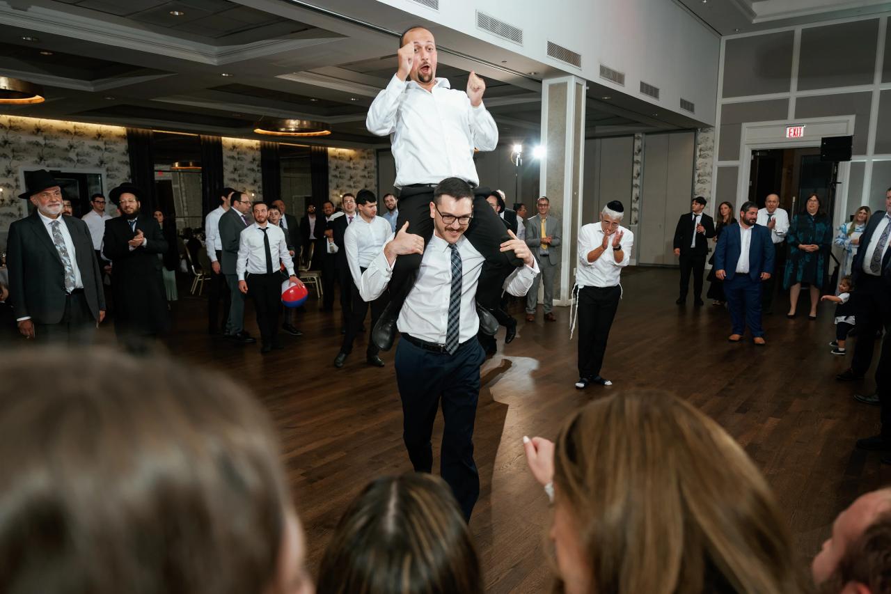Guests watching a dancing man in the middle of a reception ballroom, with energetic hand gestures and a crowd in the background.