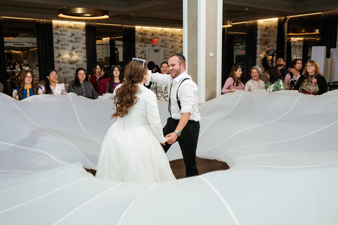 Bride and groom standing in the aisle during a traditional moment, with a long white veil filling the foreground and guests watching from both sides.