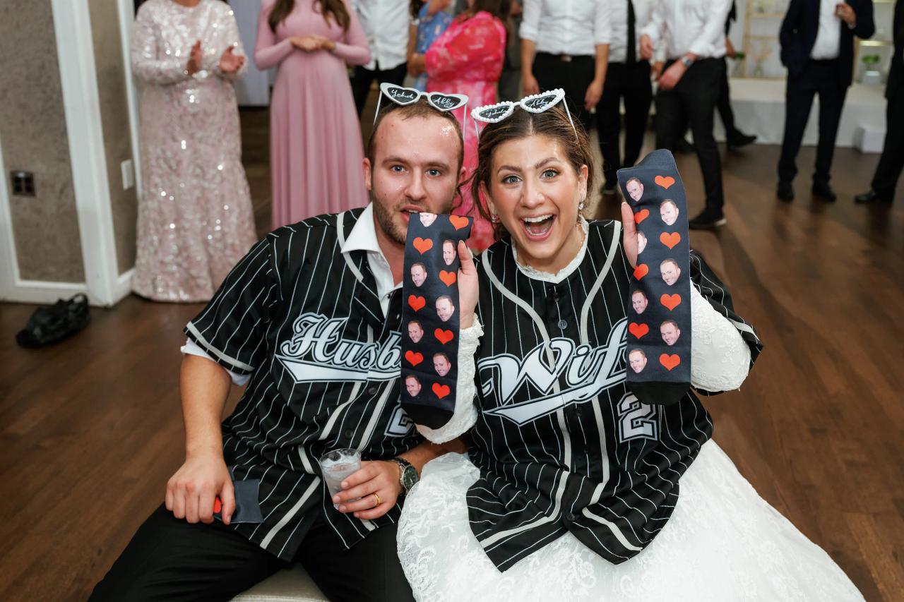 Bride and groom smiling and laughing while seated close together and holding decorated keepsake cards with hearts at a wedding reception.