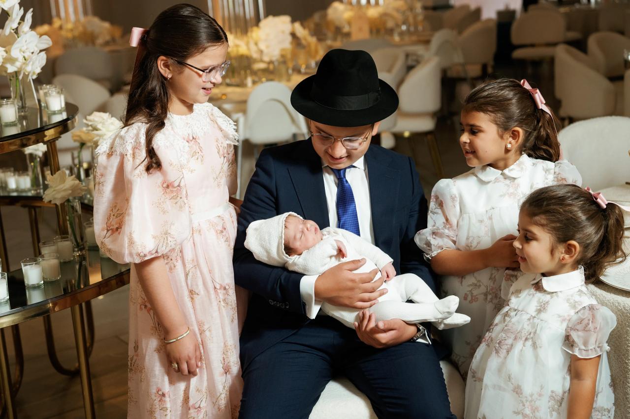 An adult seated with a baby and three children in light dresses at the celebration