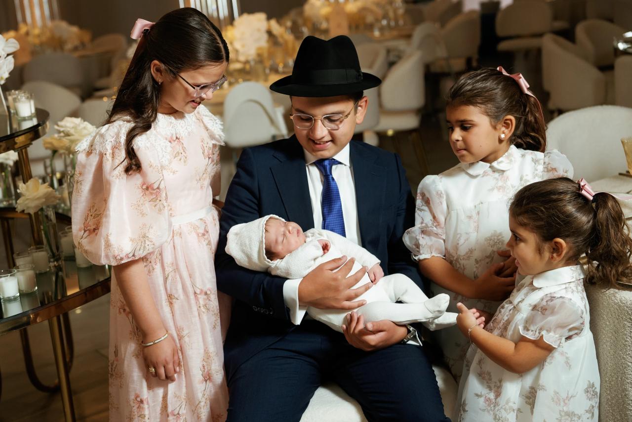 An adult holds a baby as children in coordinated light dresses gather around