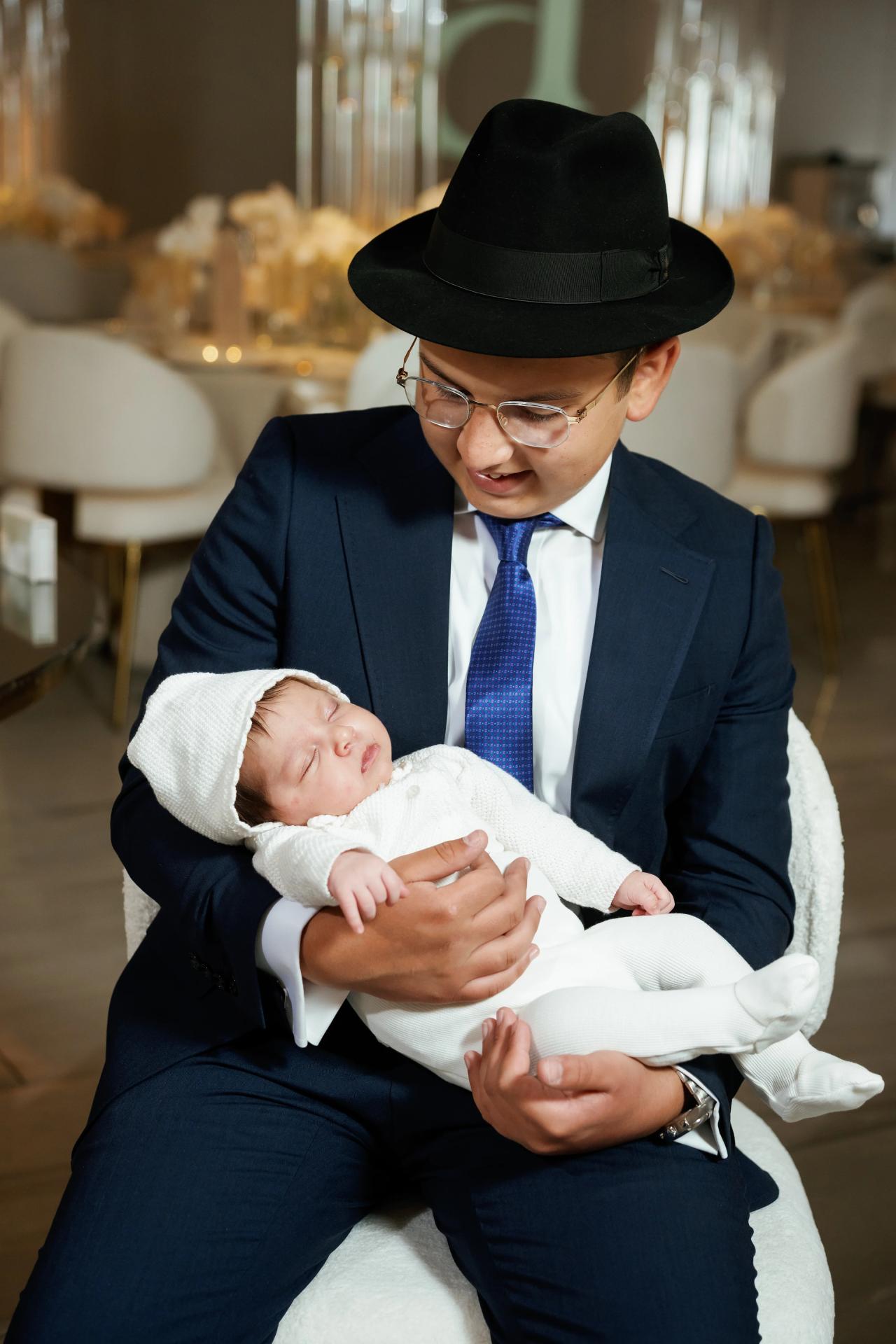 A guest in a dark suit cradles a swaddled baby at the celebration