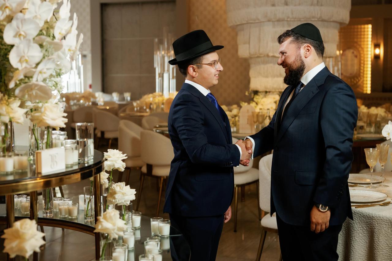 Two guests embrace beside floral centerpieces at a Bar Mitzvah reception