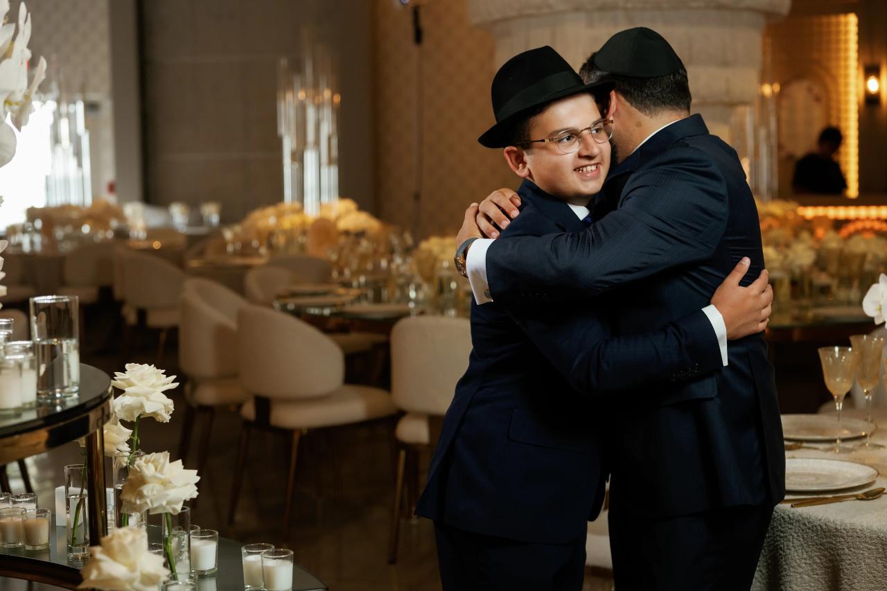 Two guests in formal attire share a smiling embrace in the reception hall