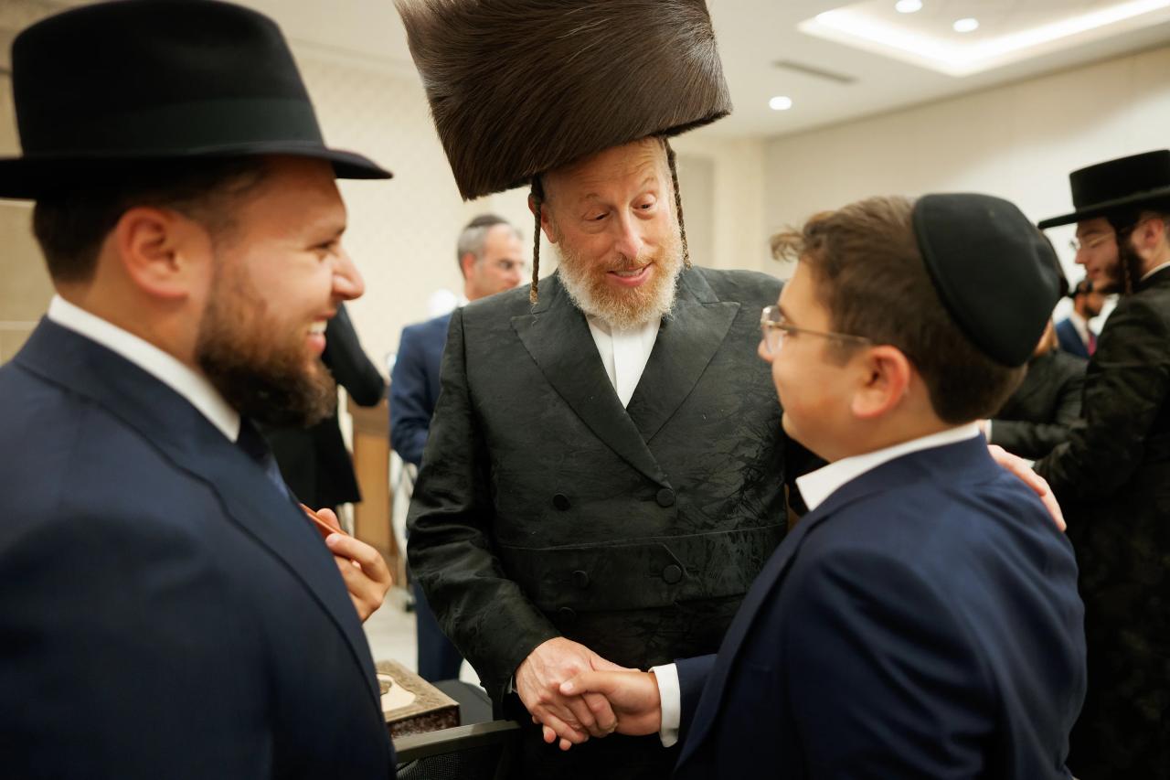 Three guests in black hats and suits greet one another at the Bar Mitzvah celebration