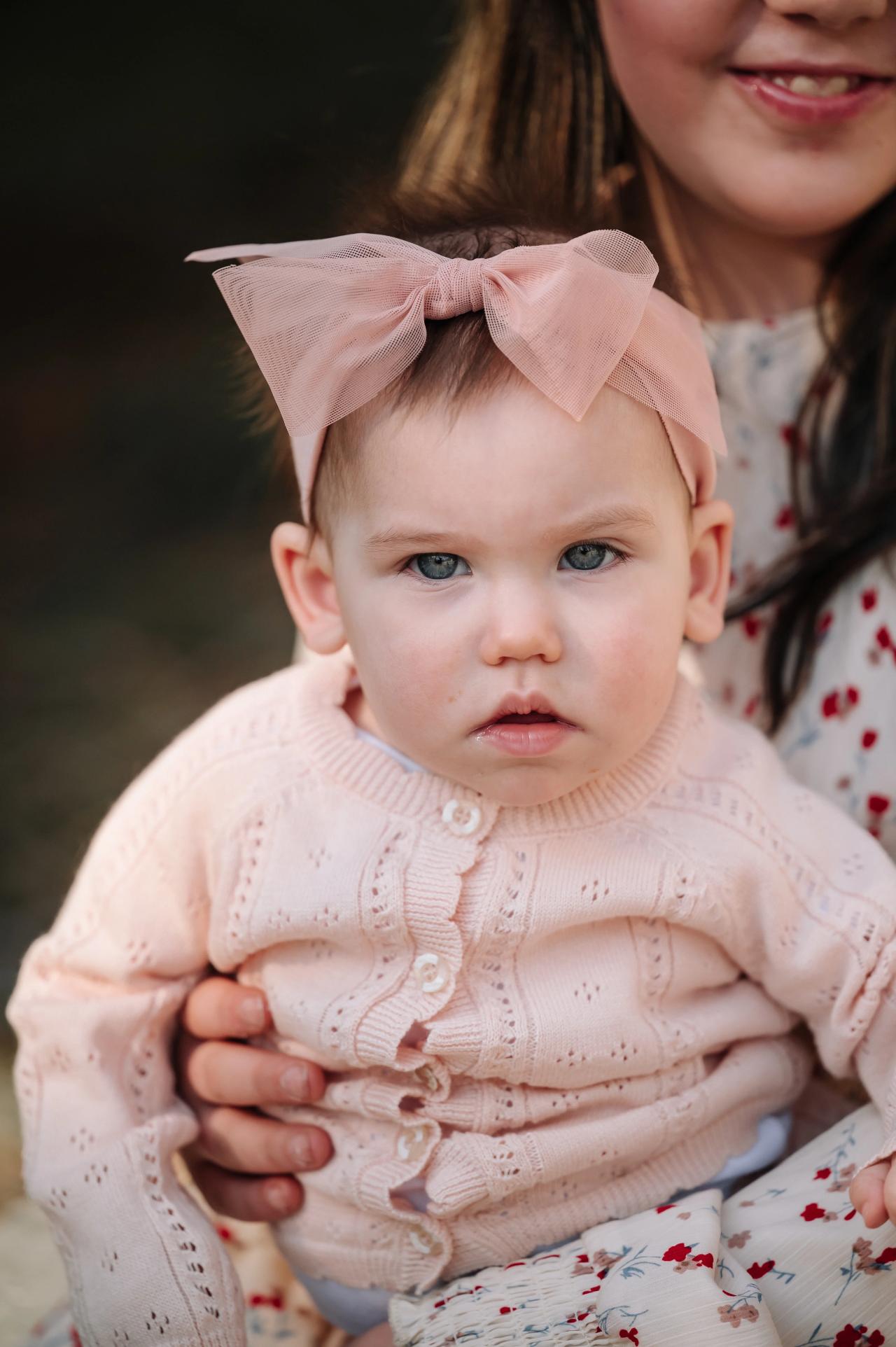 Baby wearing a pink bow held during an outdoor family portrait