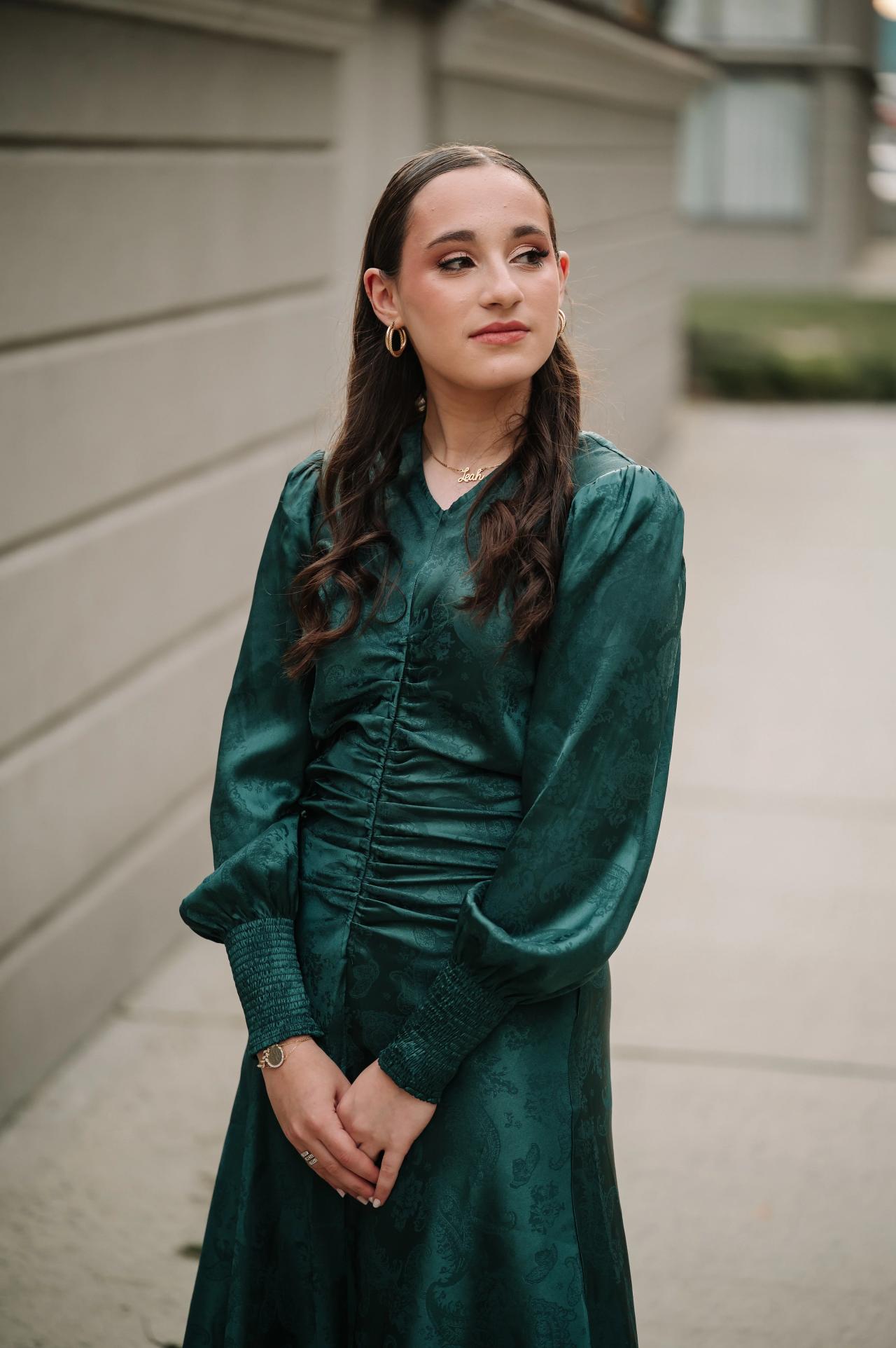 Portrait of a girl in a green dress beside a pale wall