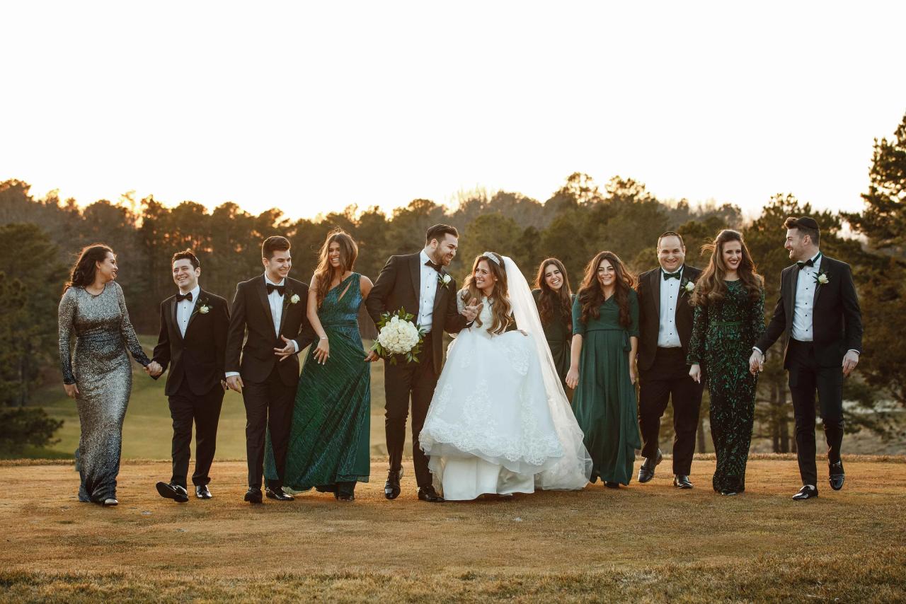 Bride and groom centered as the wedding party walks together outdoors at sunset, surrounded by smiling family and friends on a grassy field.