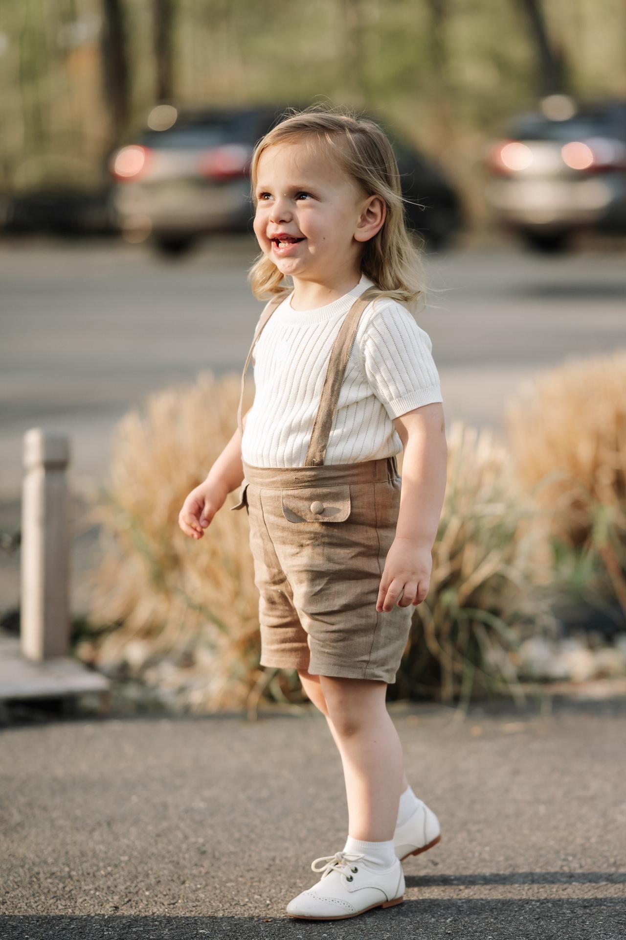 Smiling child in tan suspender shorts during an outdoor Upsherin portrait session