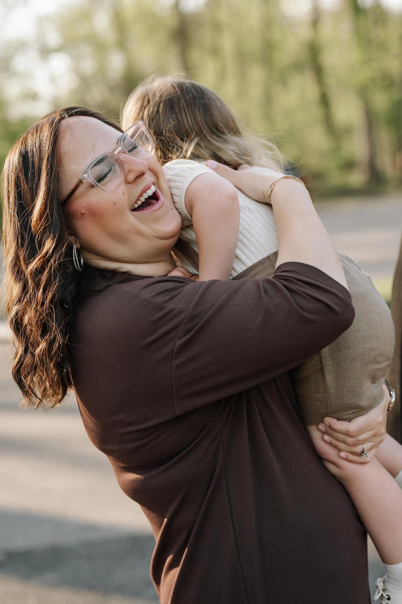 Woman laughing as she hugs a child close in the spring sunshine