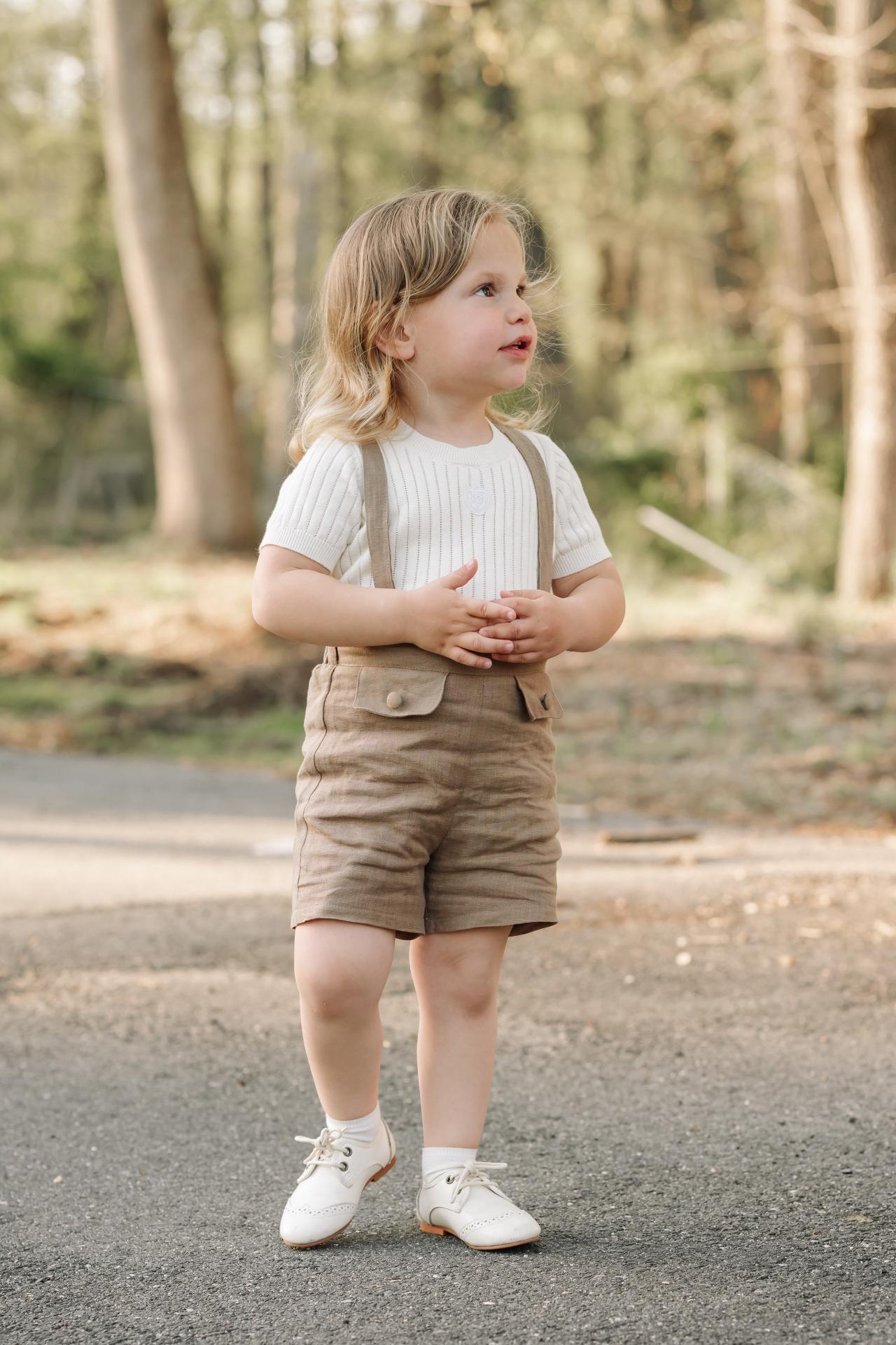 Child in tan shorts and suspenders standing on a woodland path