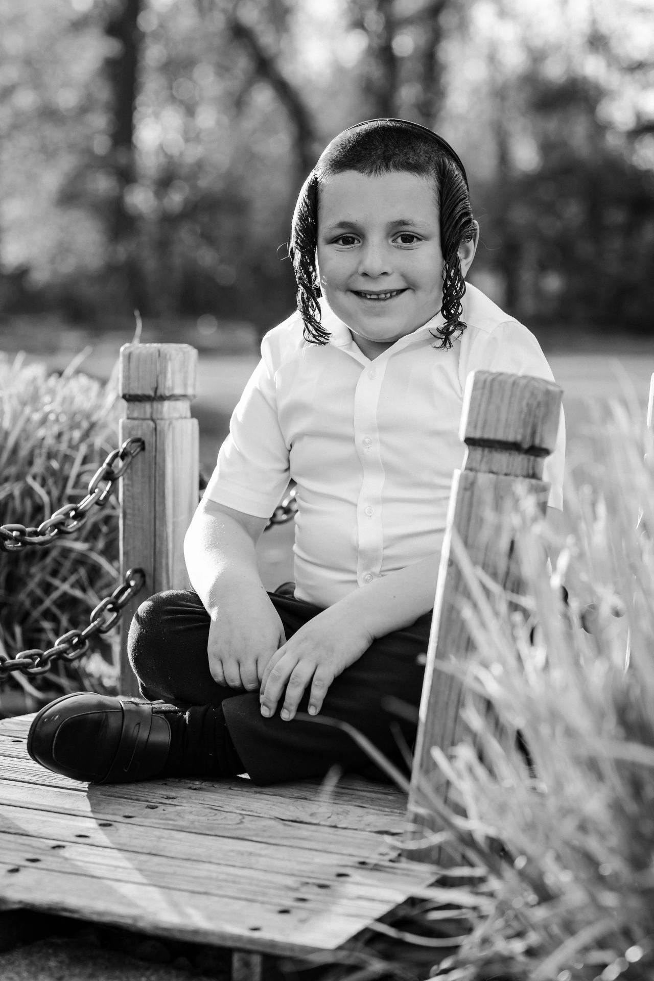 Black-and-white portrait of a boy seated on a wooden bridge