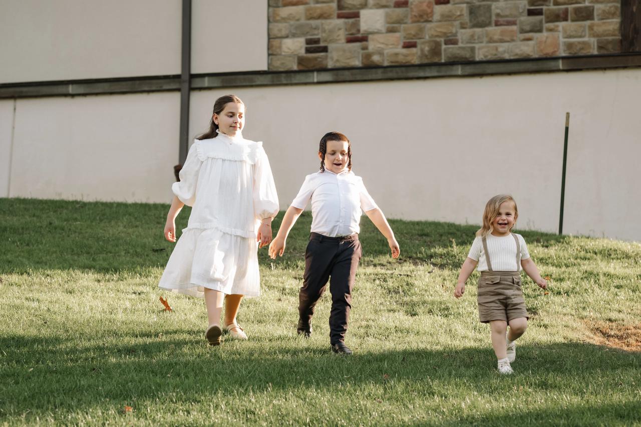 Three siblings walking together across a sunny lawn