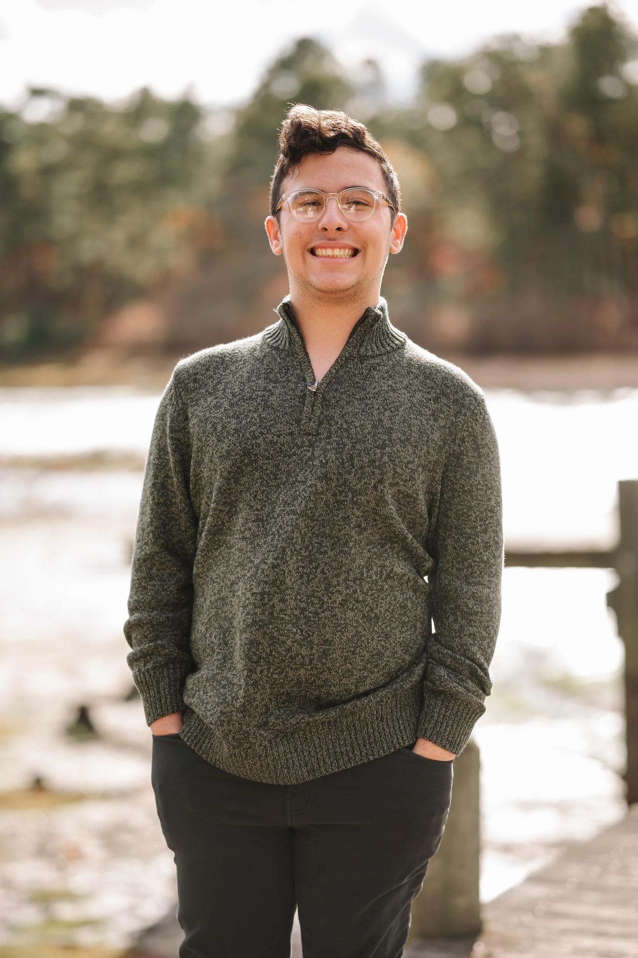 Portrait of a young man with glasses in a green sweater by the water