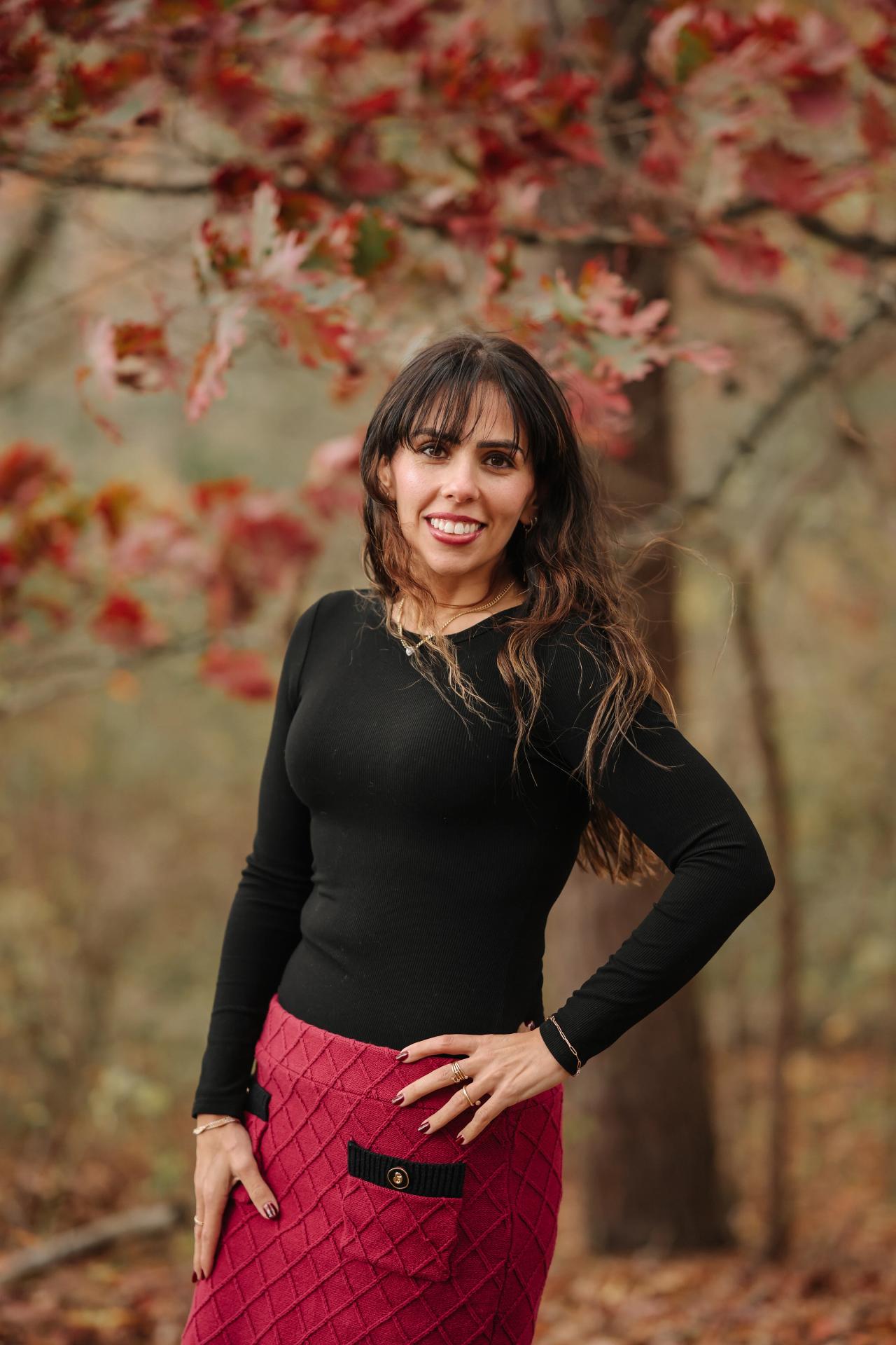 Woman smiling beneath red autumn leaves during an outdoor portrait session