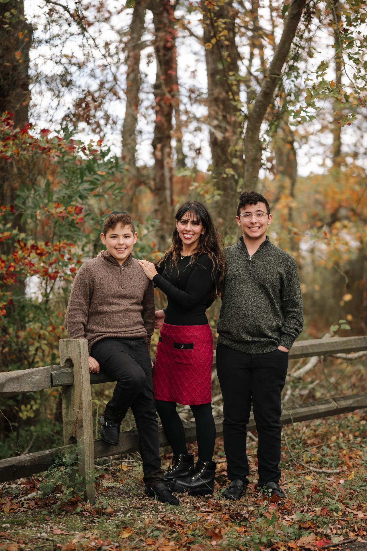 Family of three standing together beside a wooden fence among autumn trees