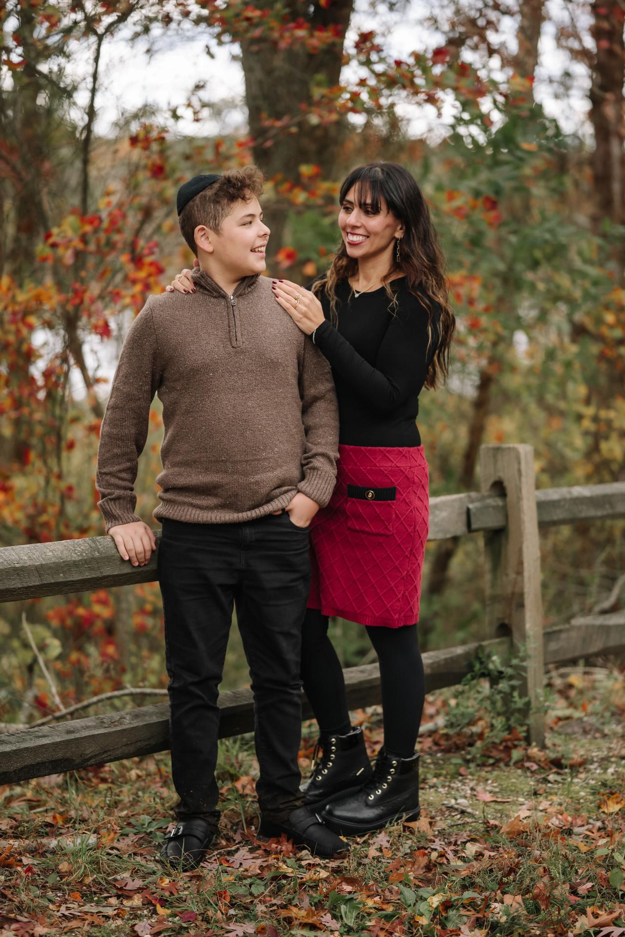 Two family members smiling at each other beside a fence in autumn woodland