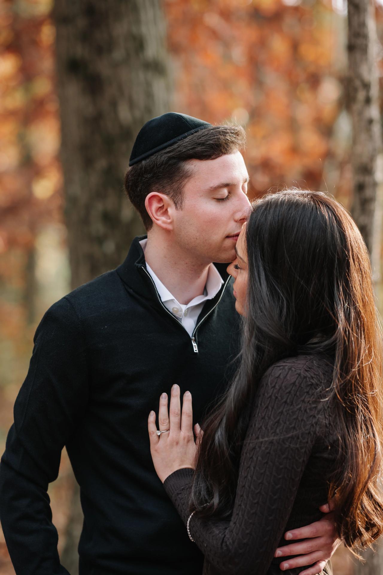 Close portrait of a man kissing his partner on the forehead among autumn trees