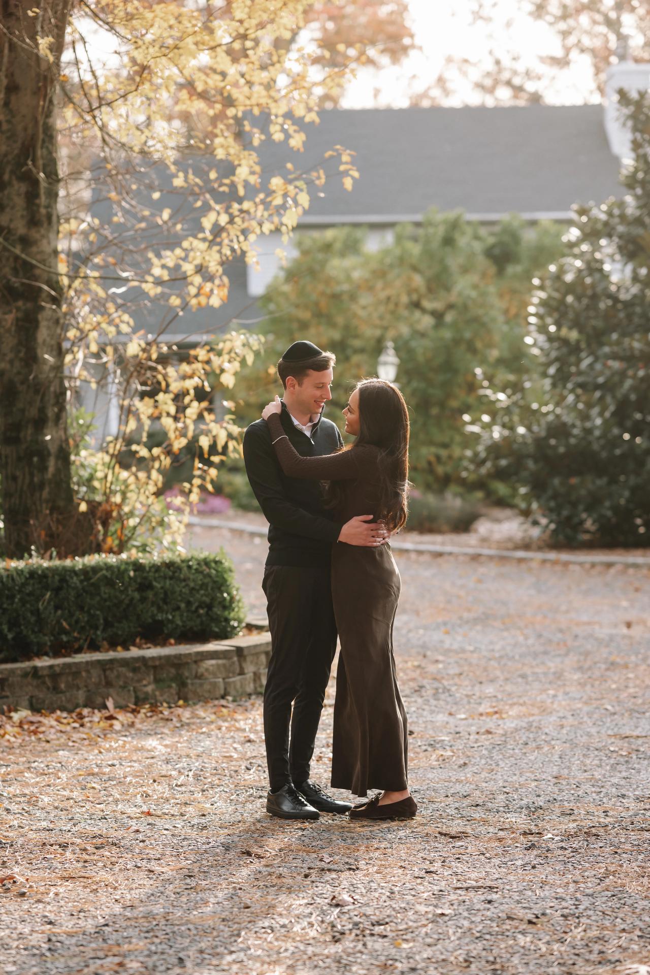 Full-length portrait of a couple facing each other beneath sunlit autumn branches