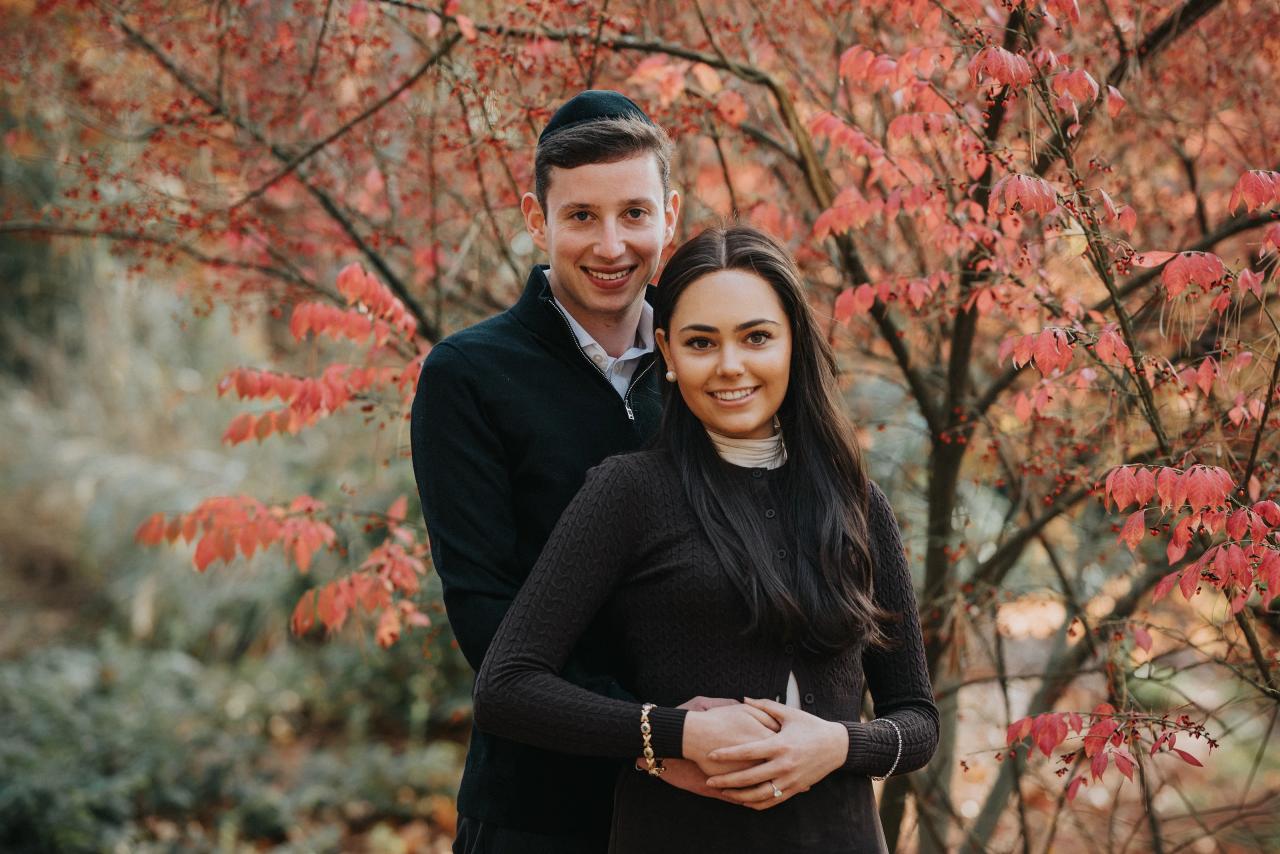 Couple standing together beneath red autumn leaves
