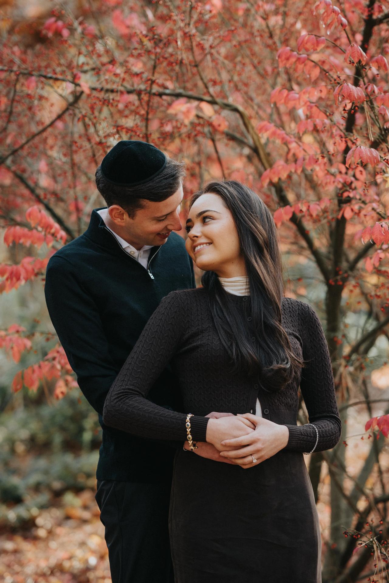 Couple sharing a smile beneath red-leaved branches