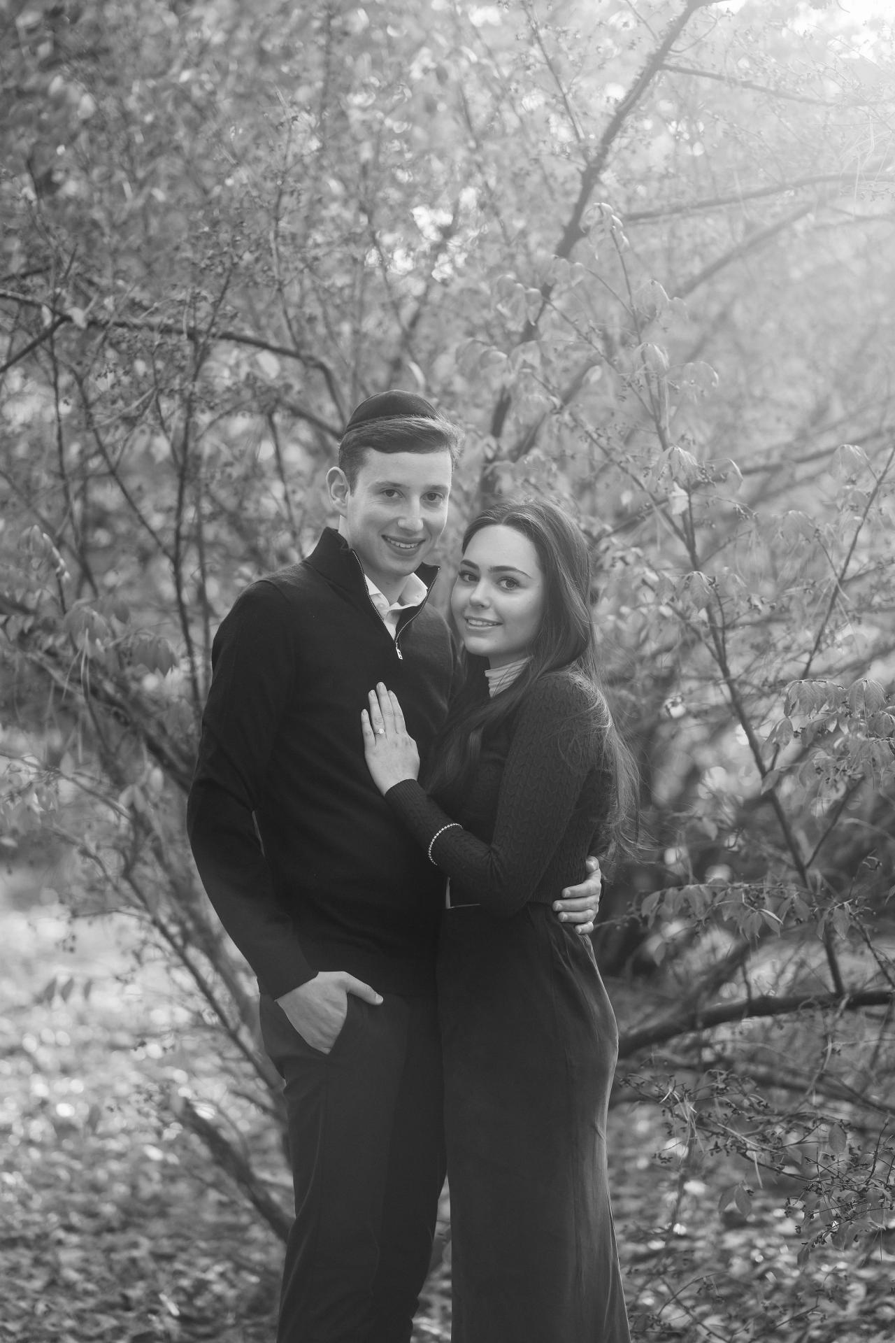 Black-and-white portrait of a couple embracing beneath autumn branches