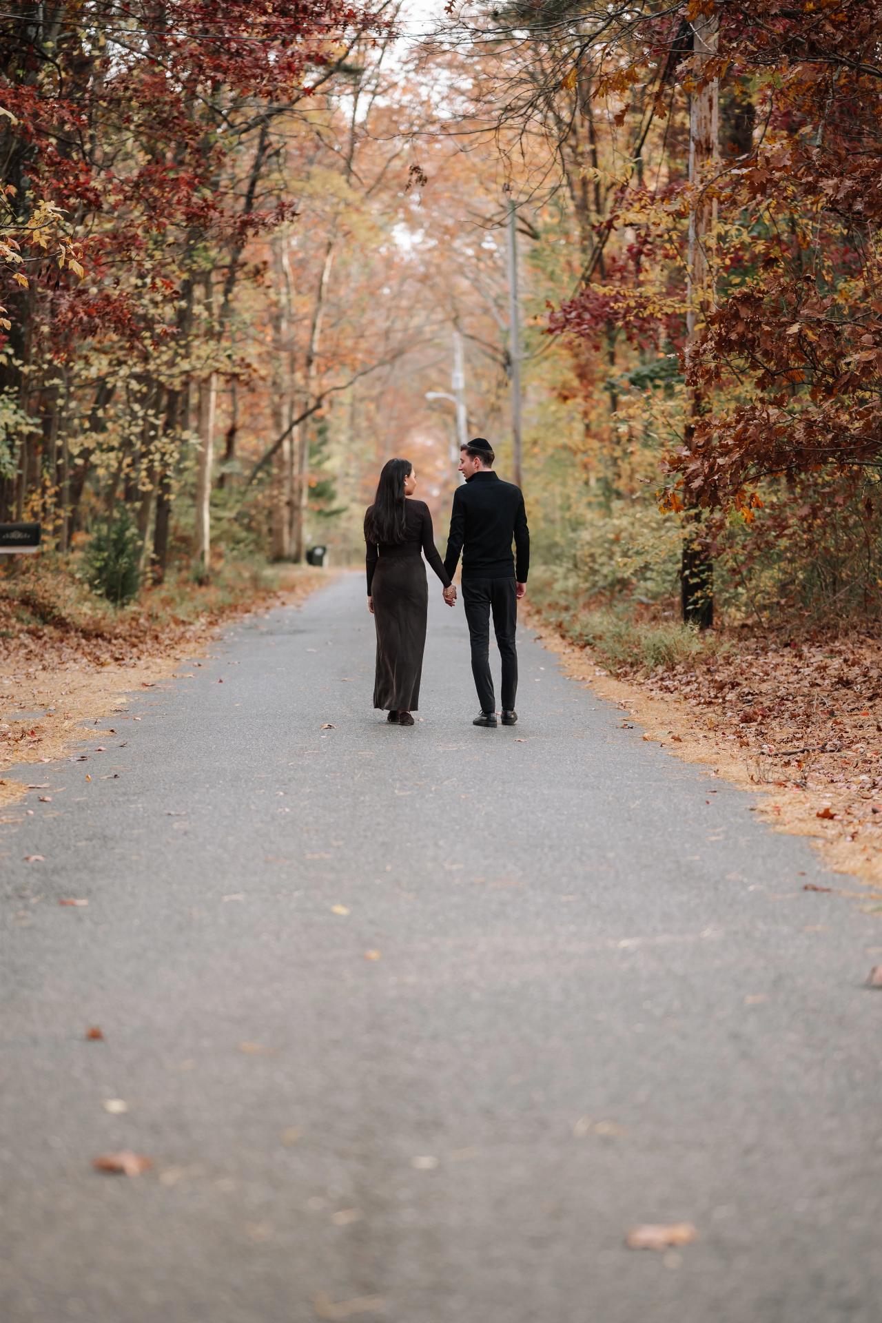 Couple walking hand in hand along a road lined with autumn trees