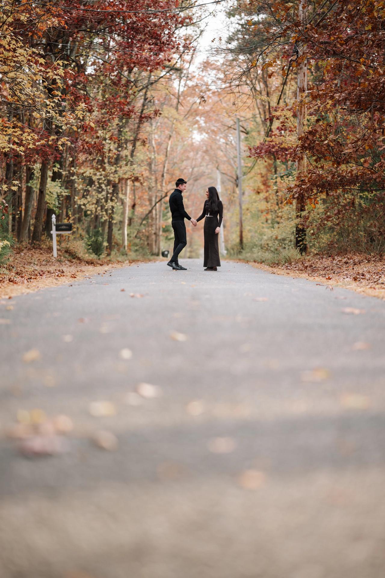 Wide autumn portrait of a couple holding hands on a woodland road