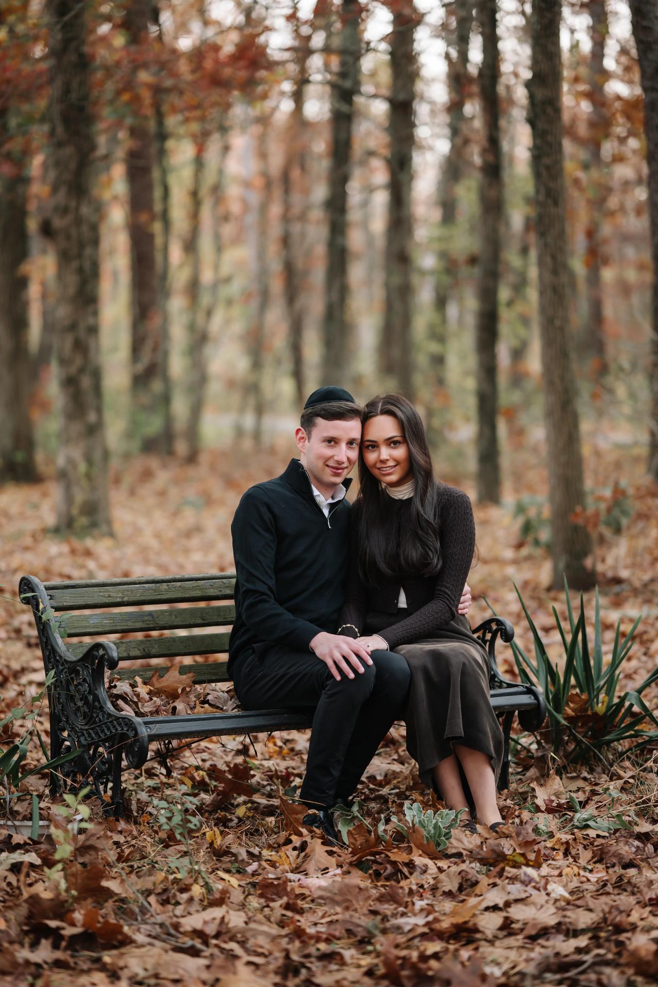 Couple smiling together on a park bench with fallen leaves around them