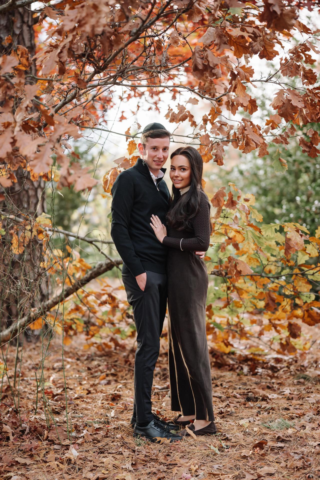 Full-length portrait of a couple beneath an arch of autumn leaves