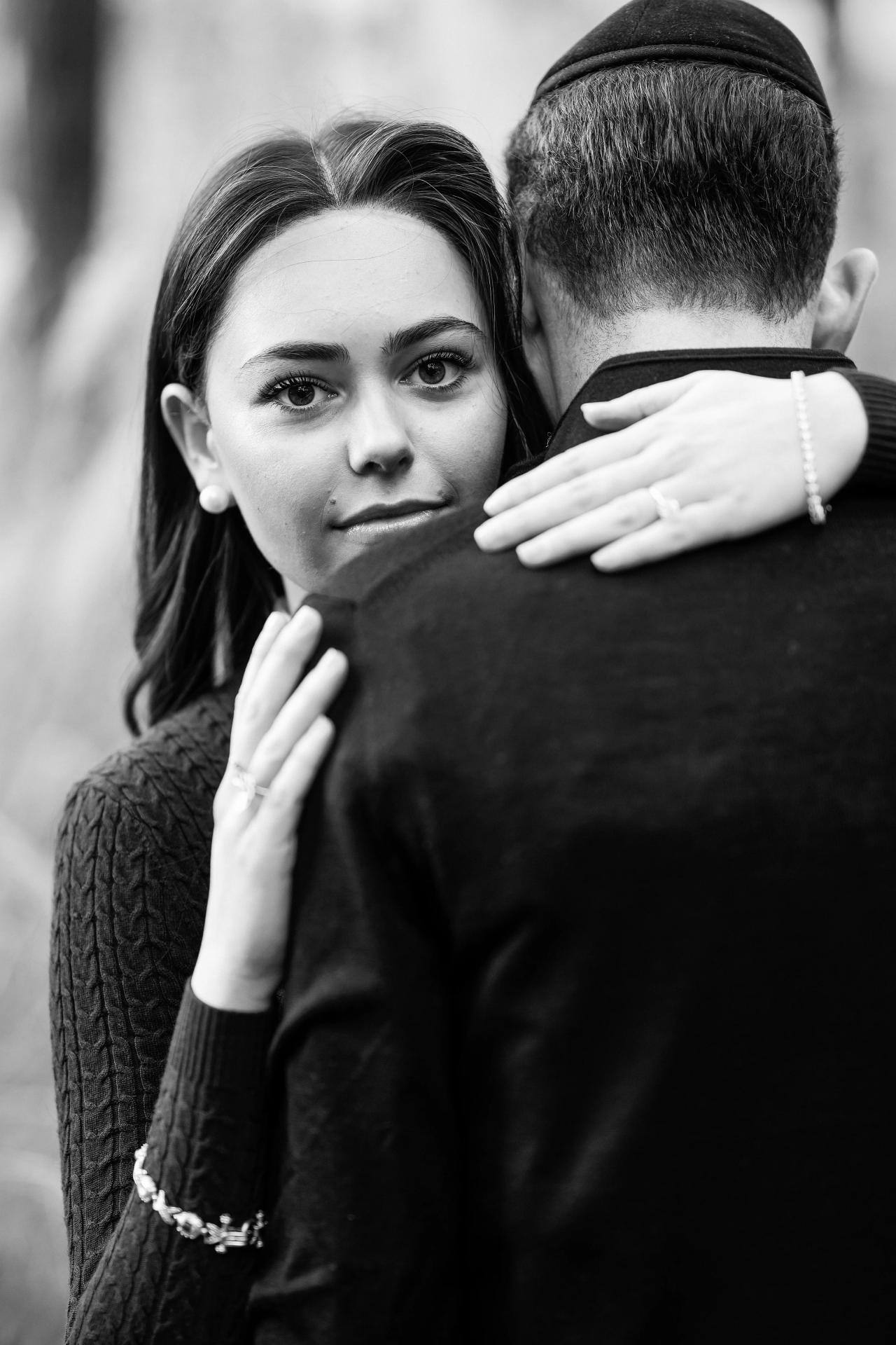 Black-and-white close portrait of a woman embracing her partner outdoors