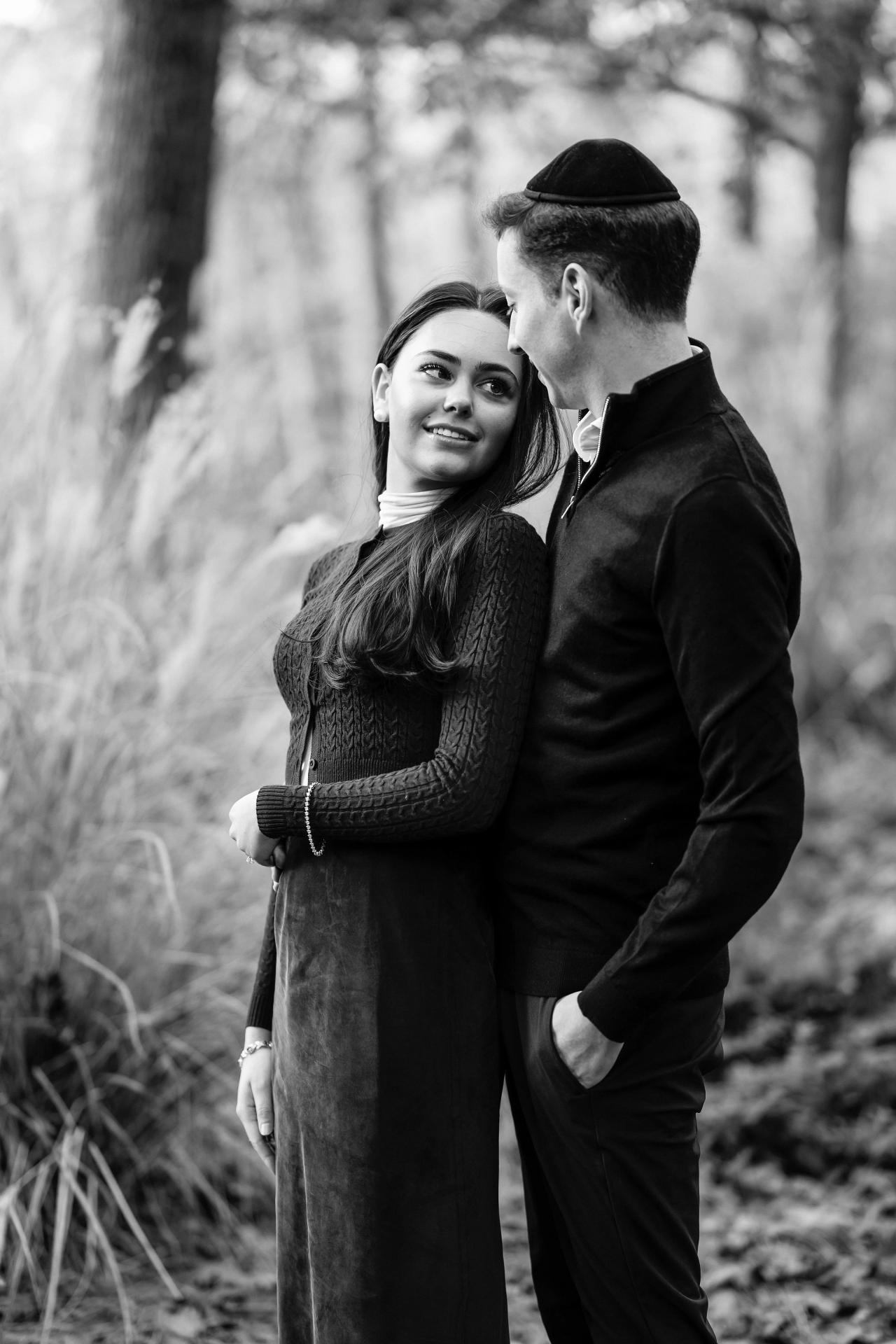 Black-and-white portrait of a couple smiling at each other in a woodland clearing